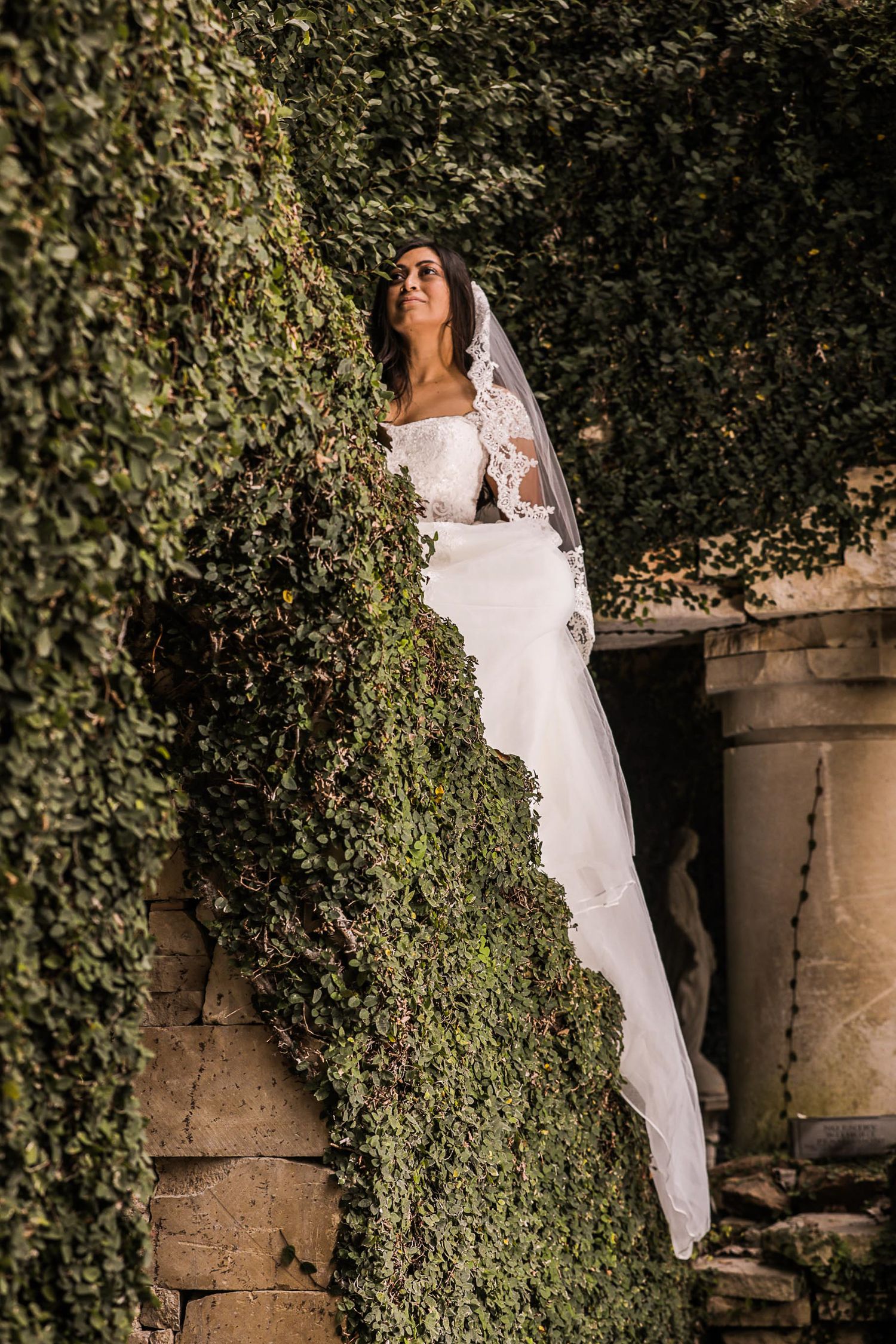A romantic bridal portrait with ivy-covered walls creating a dramatic backdrop.