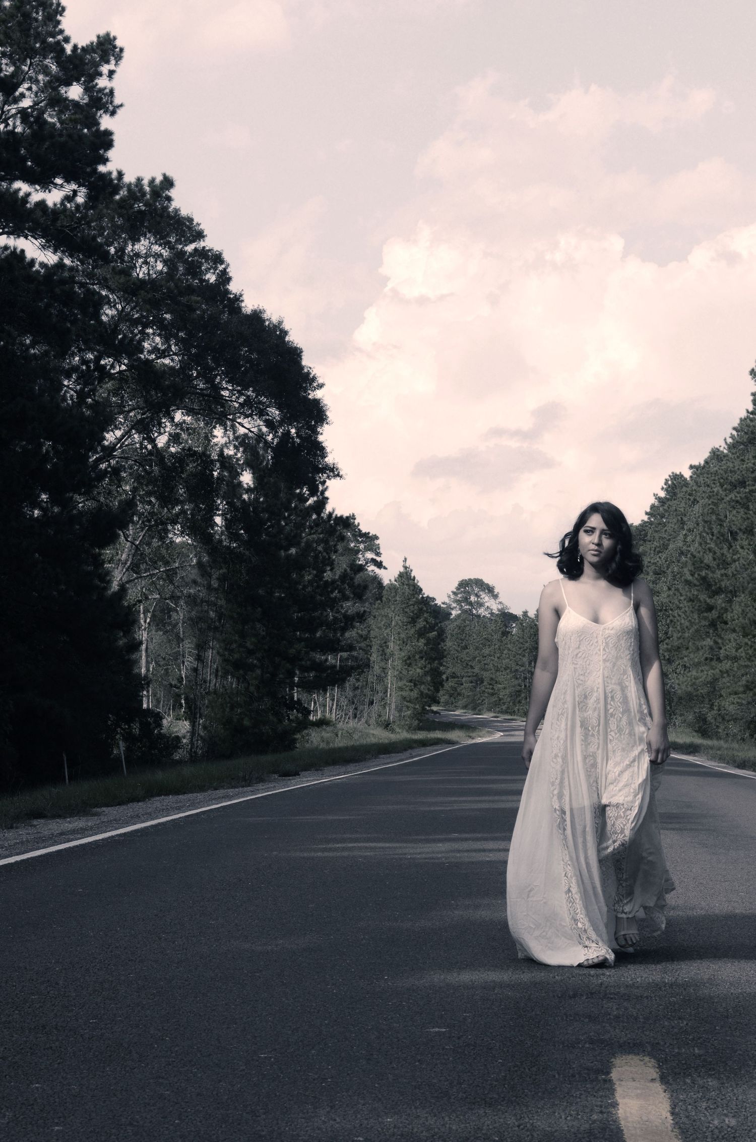 Ethereal black and white portrait of woman in flowing dress on empty road.