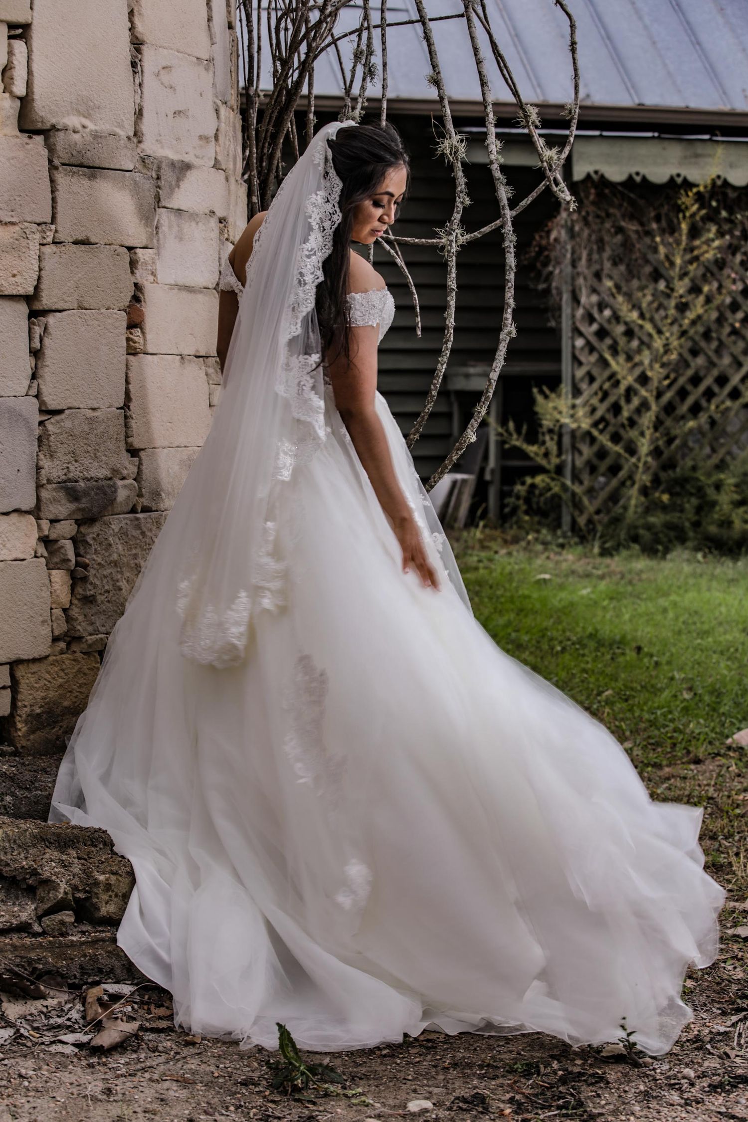 A classic bridal portrait highlighting the dramatic train of a white ballgown against stone walls.