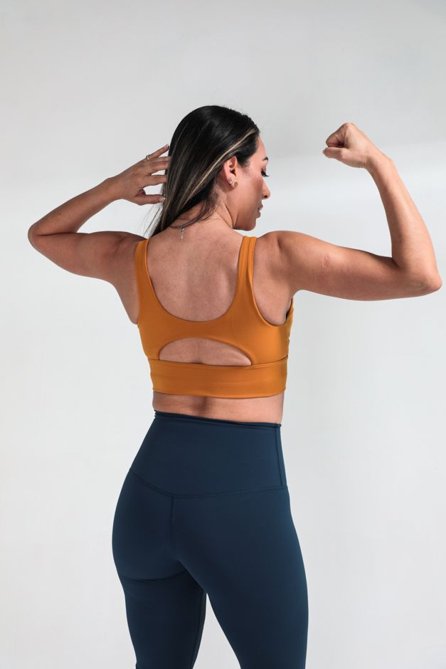 Woman in orange sports bra and navy leggings showing off athletic physique from behind.
