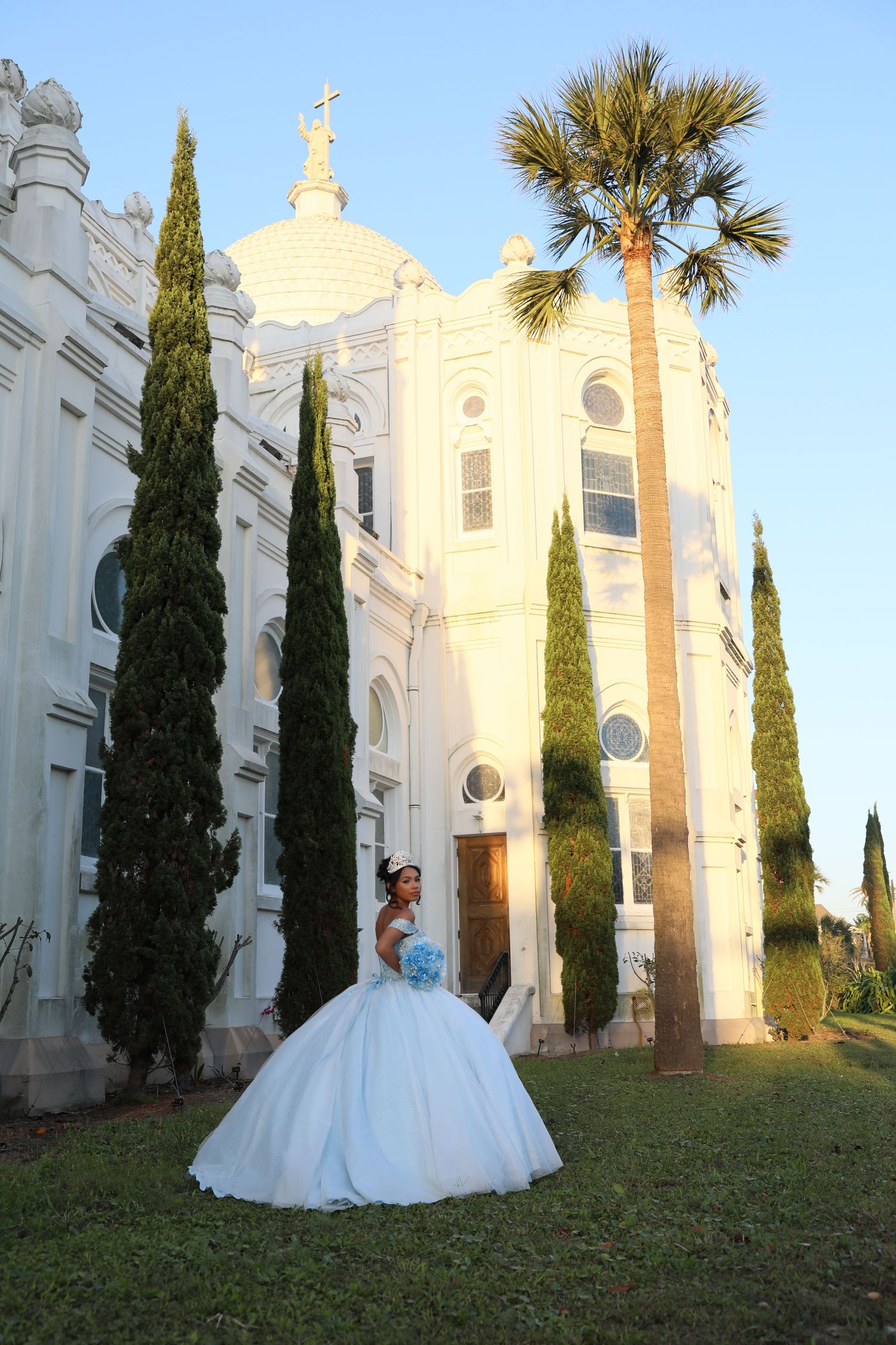 Classic white ballgown photographed in front of a grand white church with cypress trees.