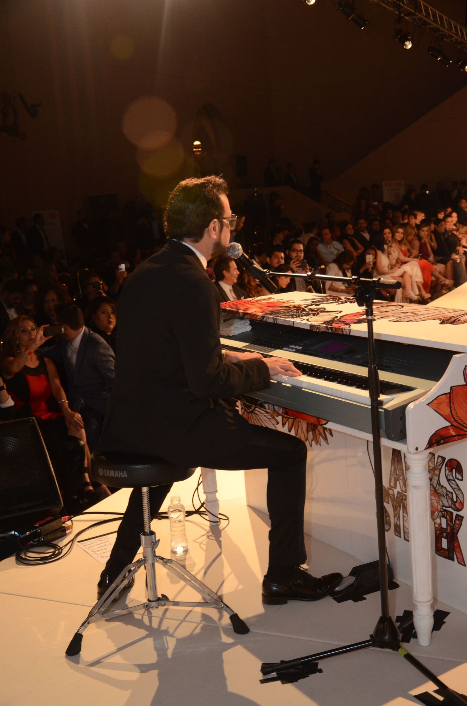 Pianist performing at fashion show on illuminated white stage.