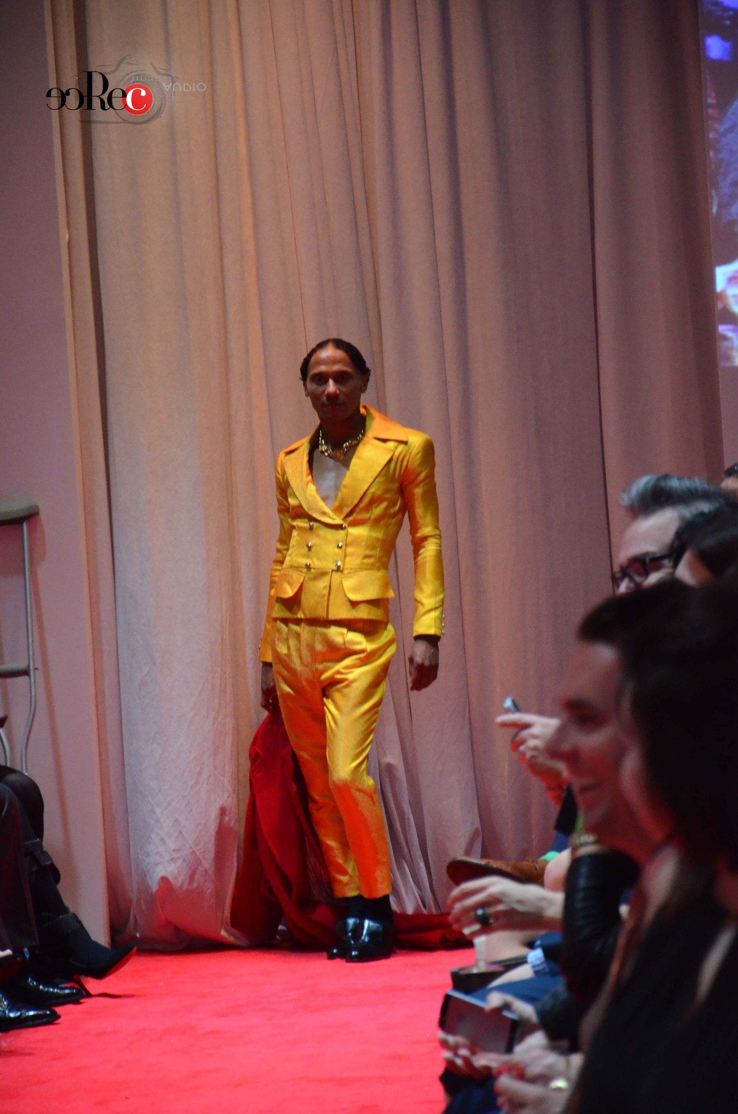 Model wearing bright yellow suit walks runway at fashion show.