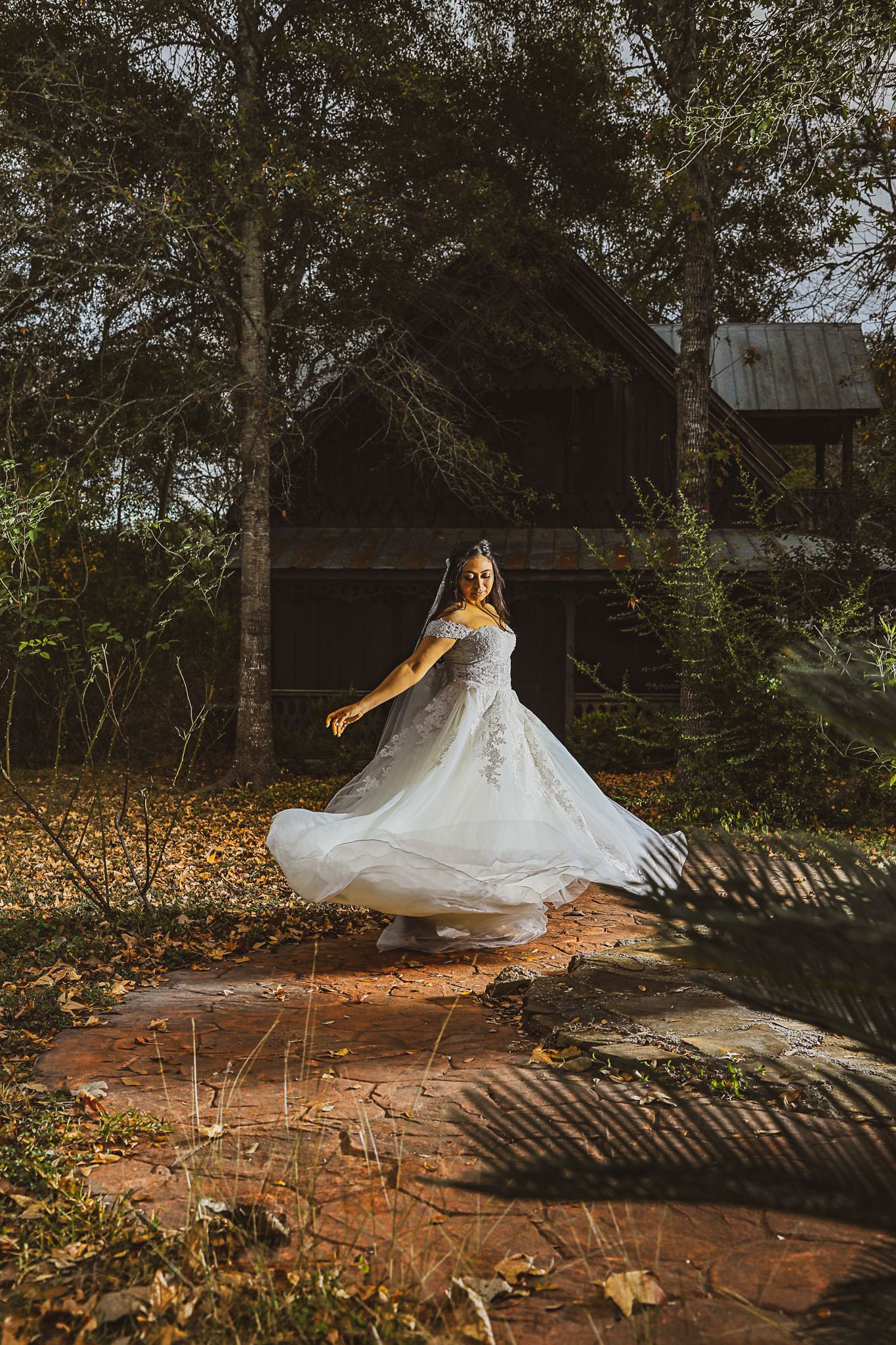 A flowing white wedding dress twirls gracefully against a rustic barn backdrop with autumn leaves scattered on the ground.