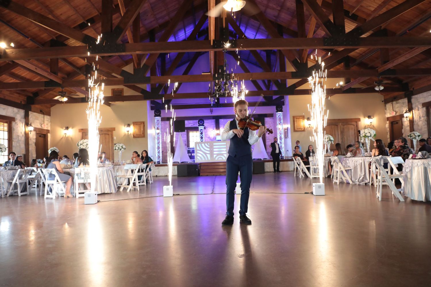 An empty wedding reception venue with sparkler fountains and purple lighting.