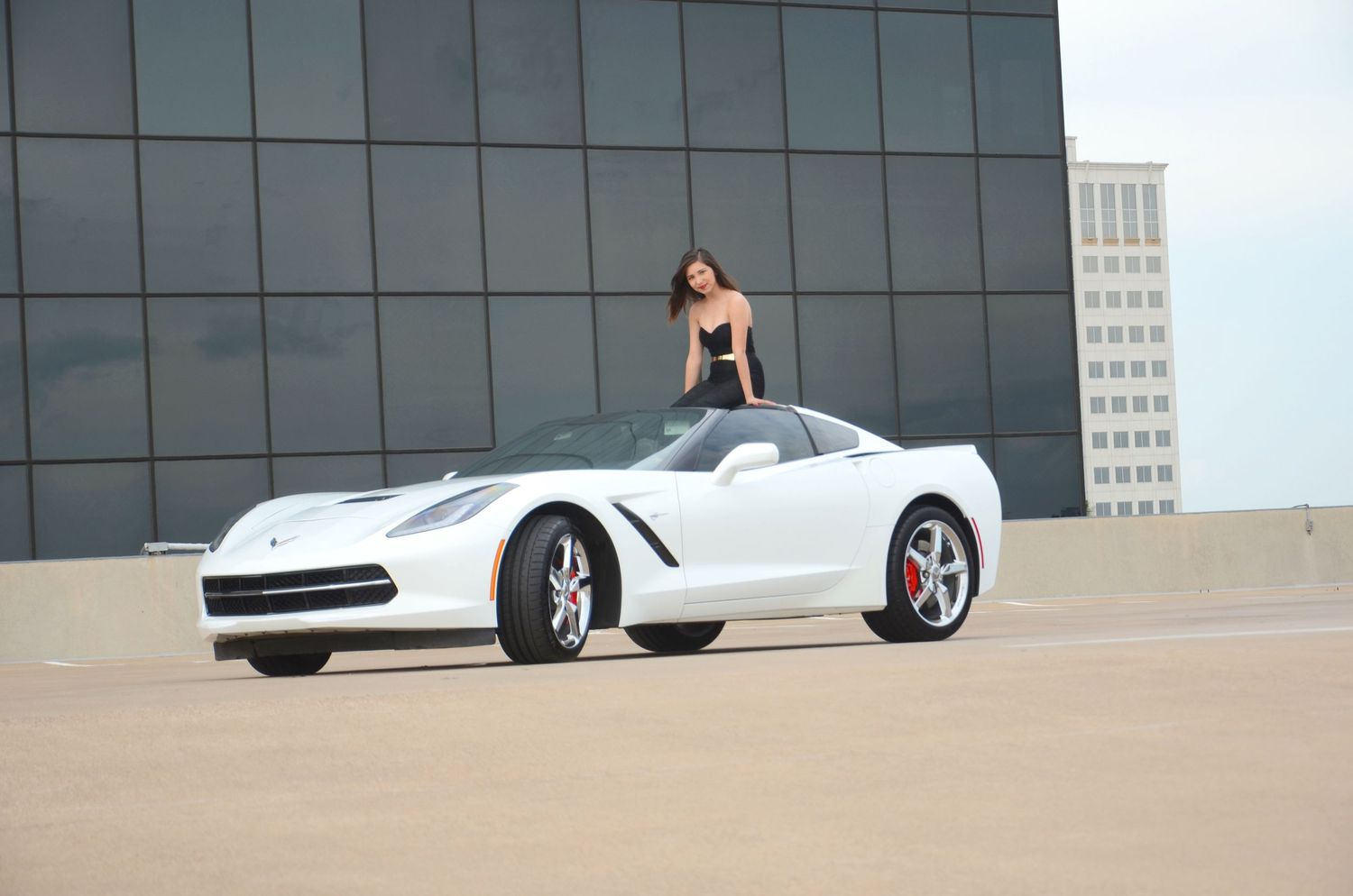 White Chevrolet Corvette parked in front of modern glass building with reflective panels.