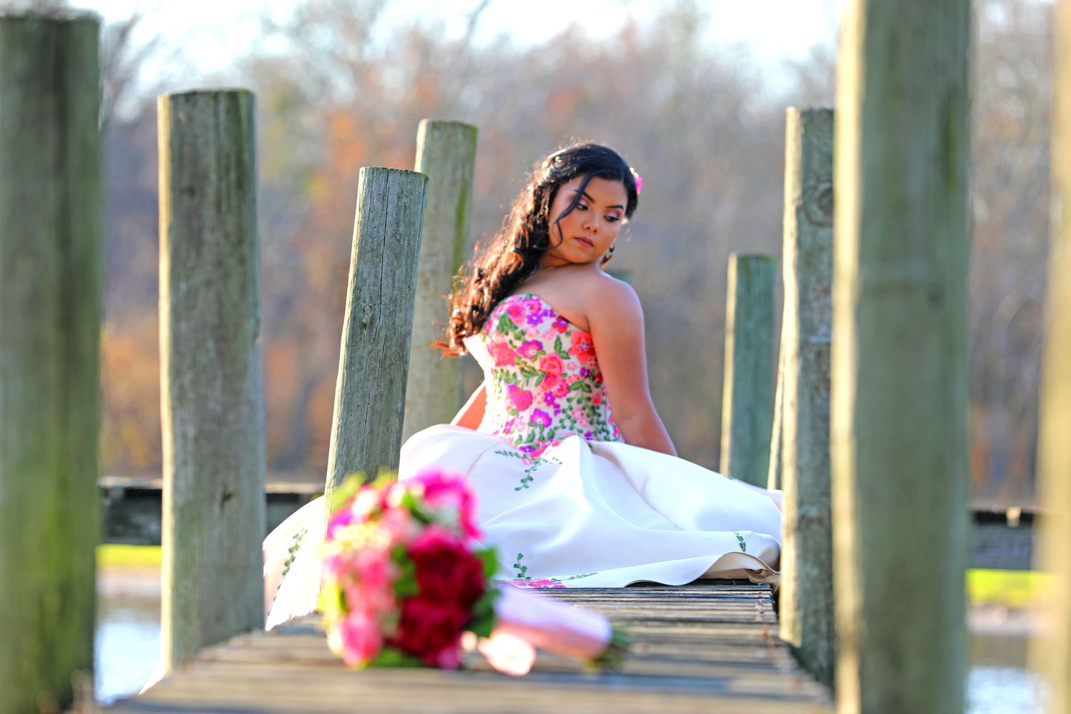 White ball gown with floral details photographed on wooden dock with bouquet.