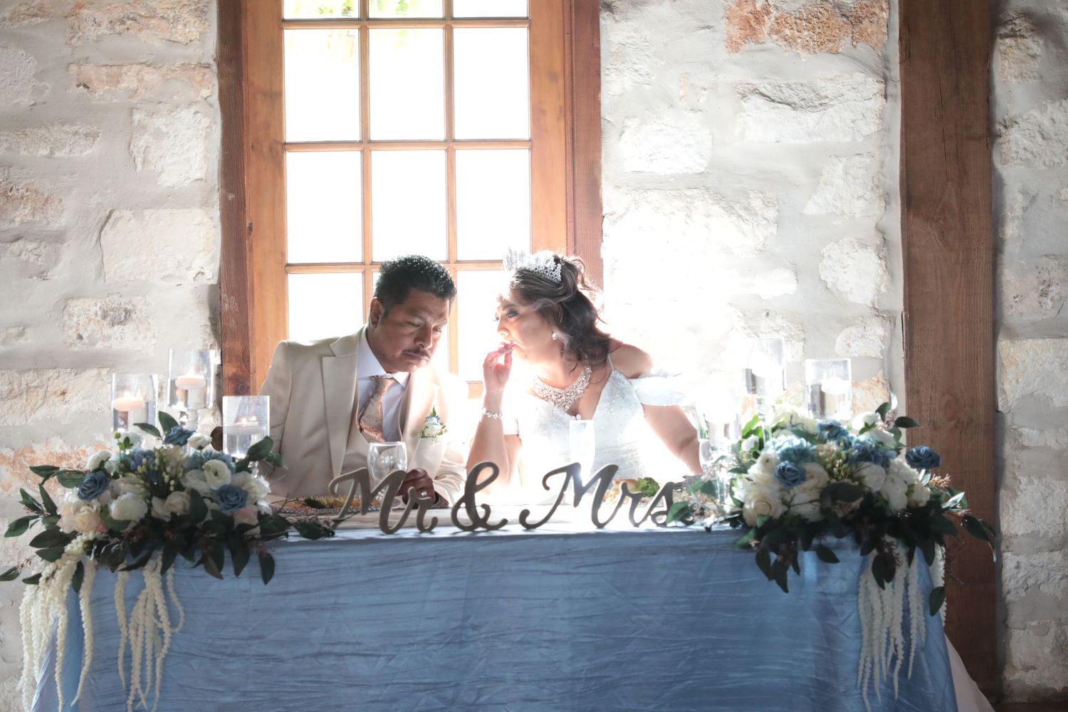 A couple sits at their sweetheart table decorated with floral arrangements and Mr & Mrs sign.