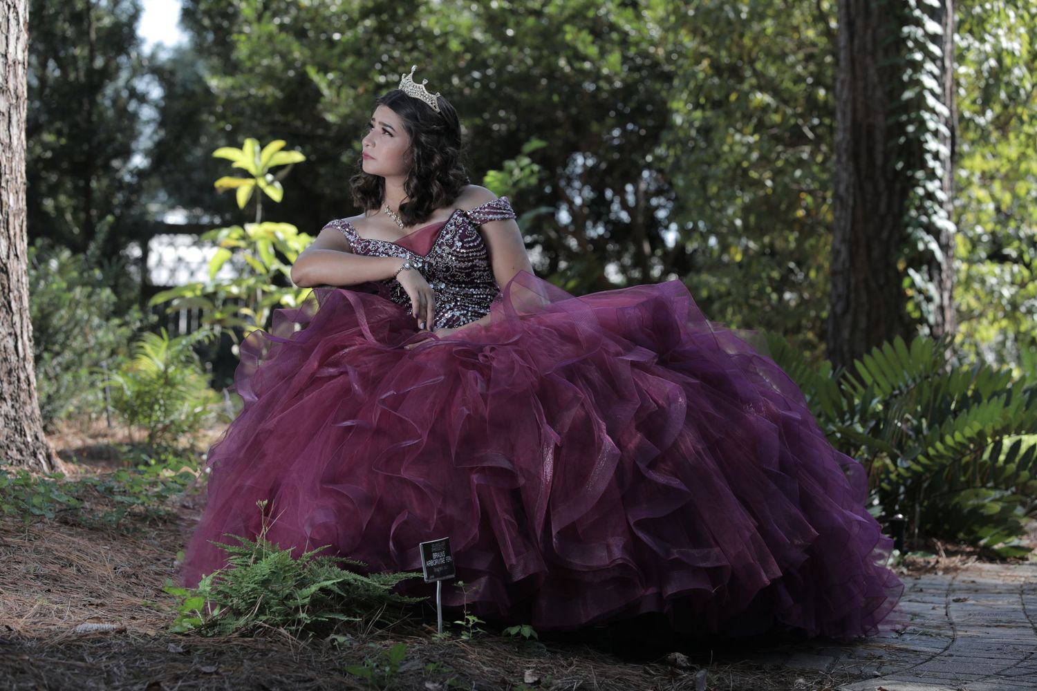 A person in a deep purple tulle gown sits gracefully in a peaceful garden setting.