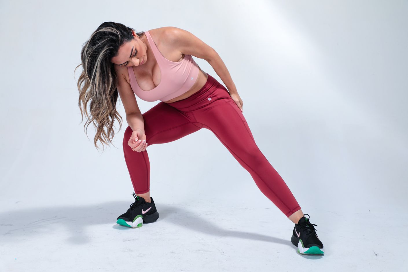 Athlete in red leggings and tank top stretches in dynamic pose against white background.