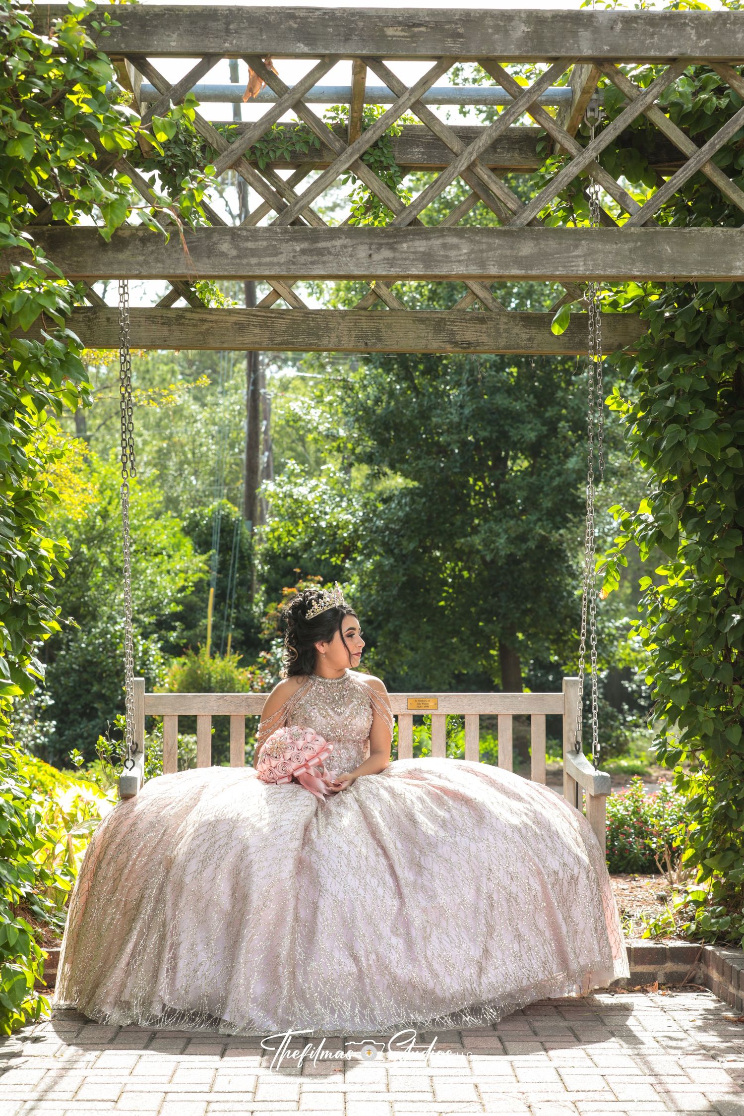 Ornate white ball gown photographed under wooden garden pergola with greenery.