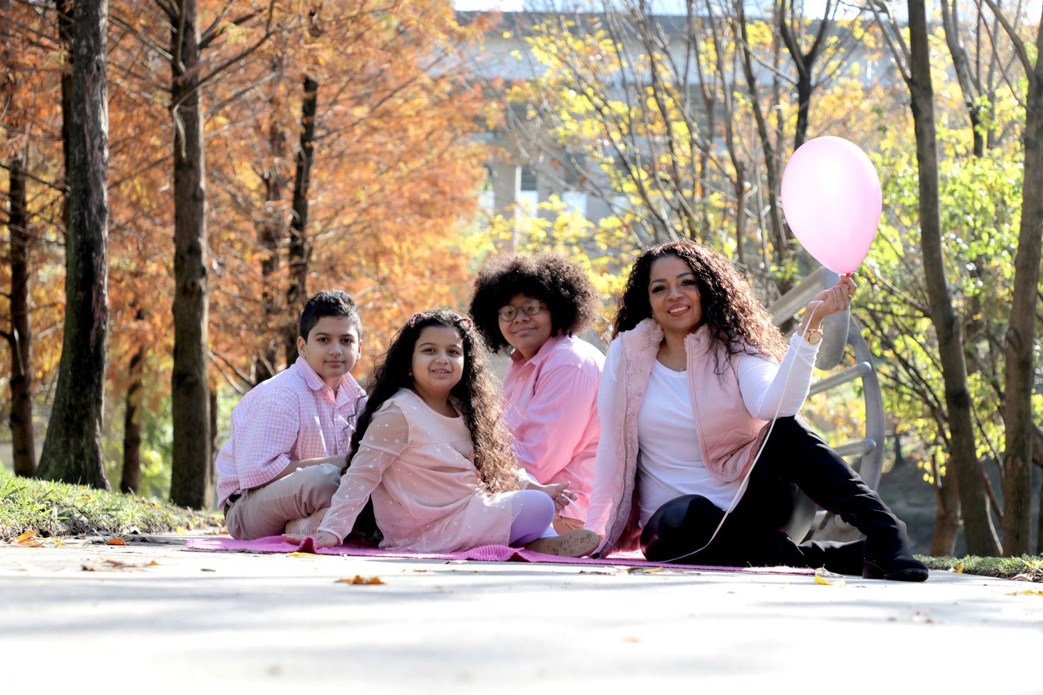 Group wearing pink outfits having a picnic under fall trees with a balloon.
