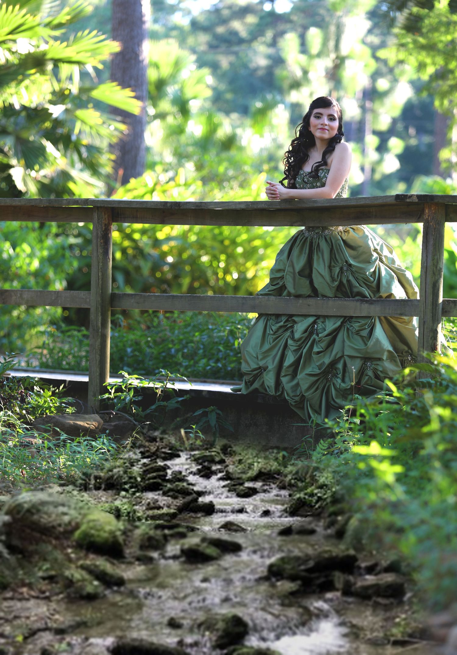 Dramatic green ballgown photographed on a wooden bridge over a forest stream.