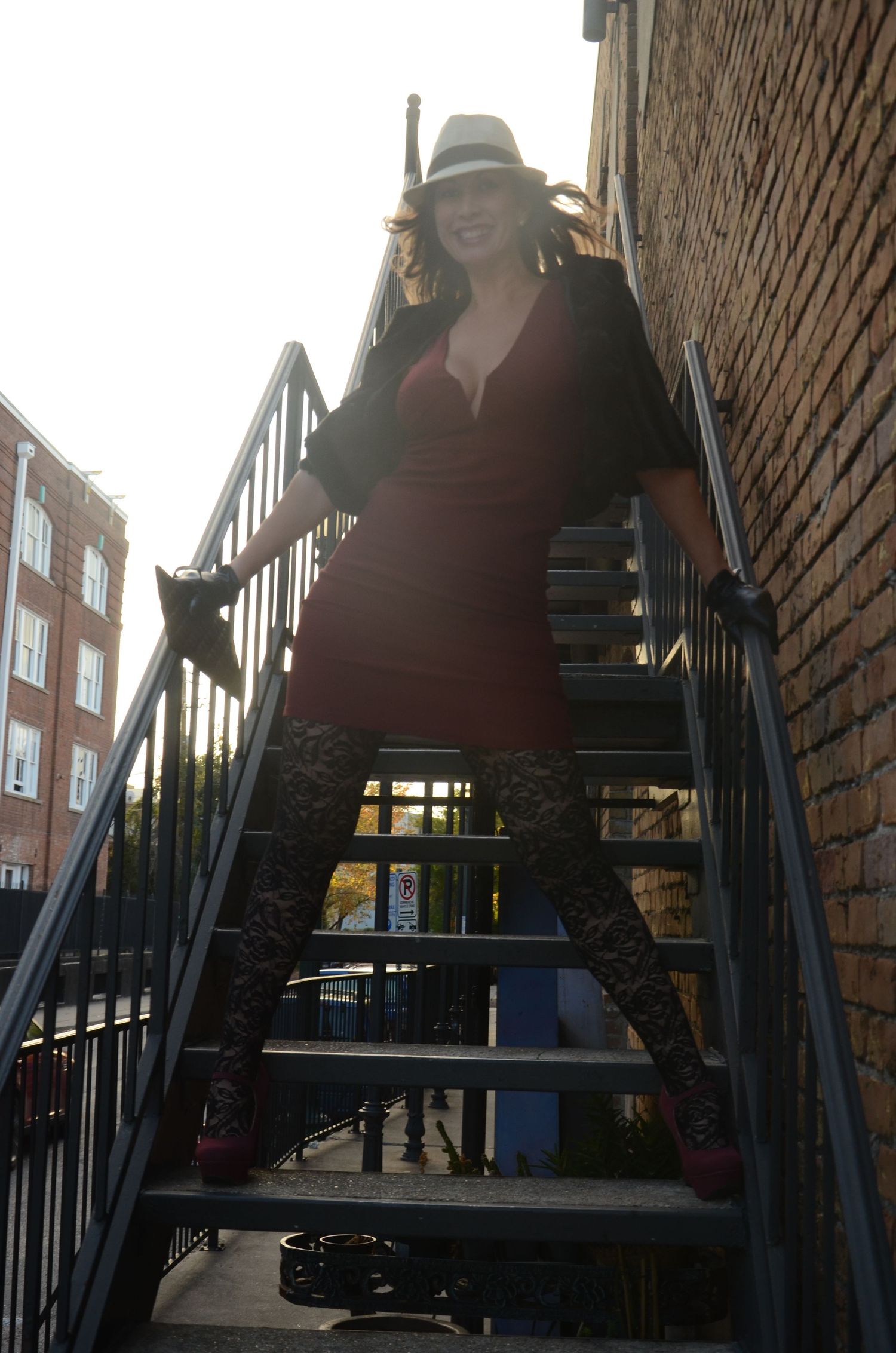 Artistic portrait on metal staircase with sunlight and brick wall background.