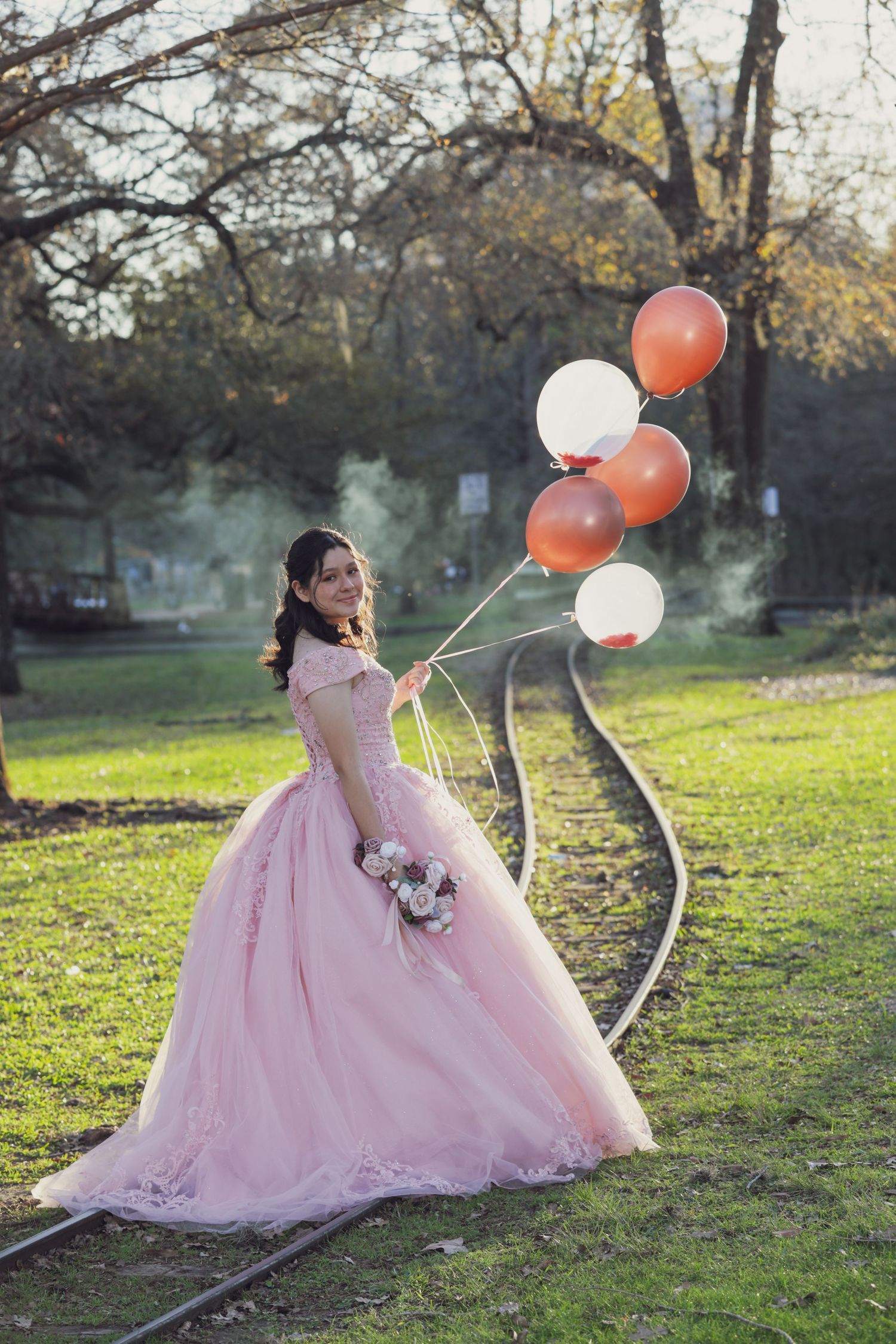 Pink princess ball gown with balloons photographed on railroad tracks at sunset.