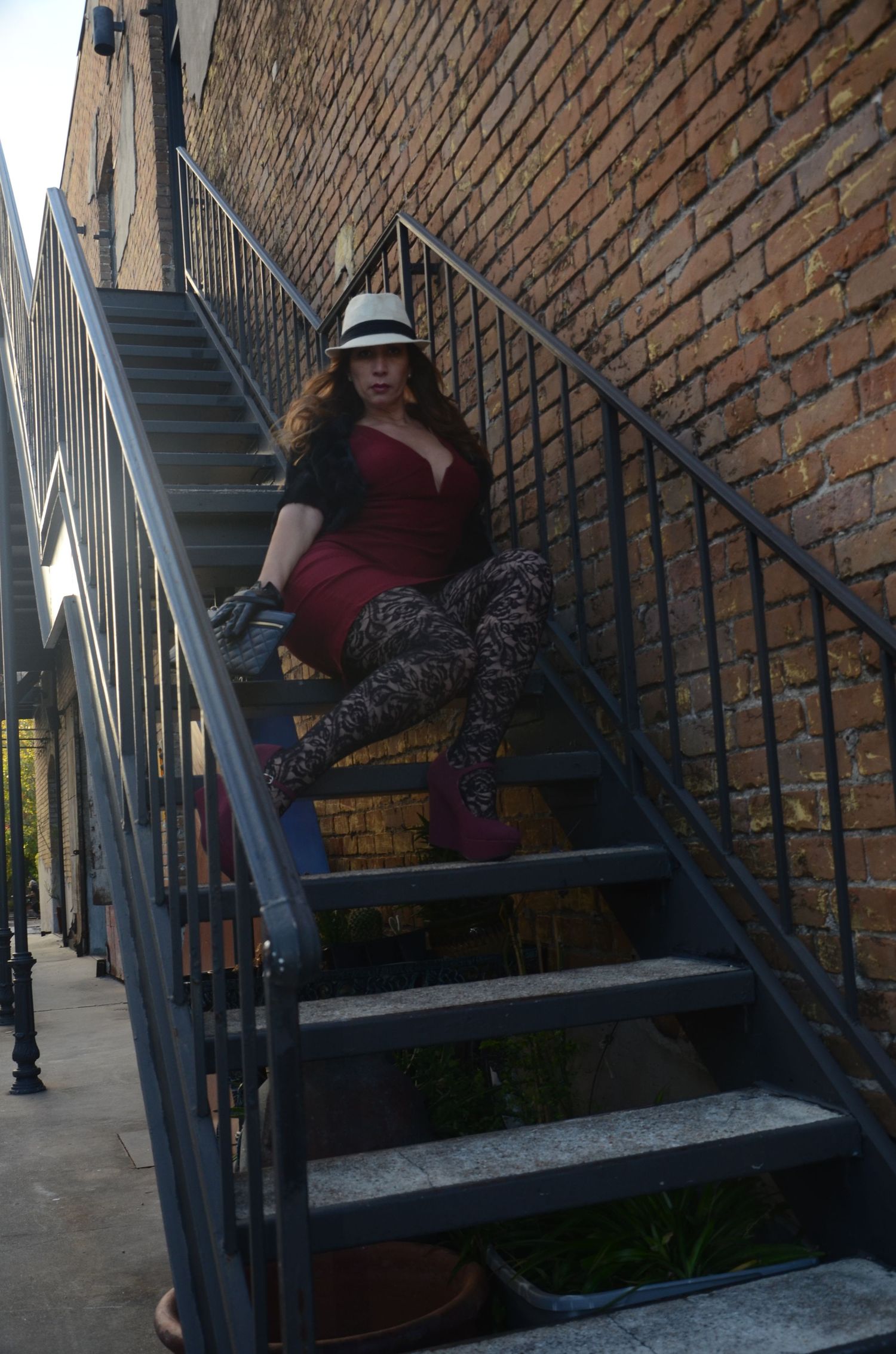 A woman in a red top and patterned pants poses on industrial metal stairs.