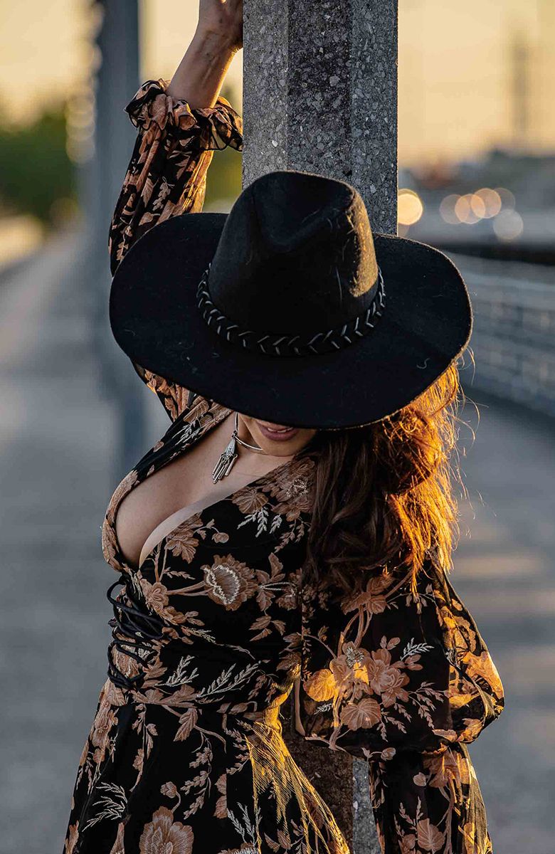 Artistic portrait featuring black cowboy hat and floral dress at golden hour.