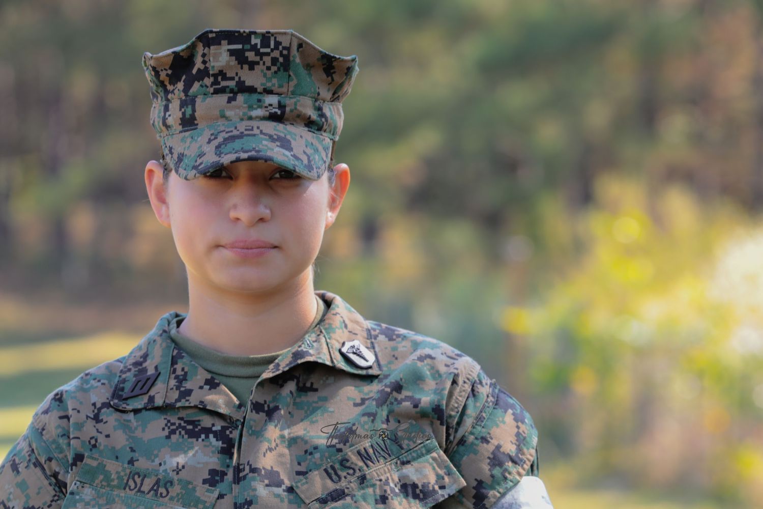 Military service members in camouflage uniforms and caps stand together outdoors during daytime.