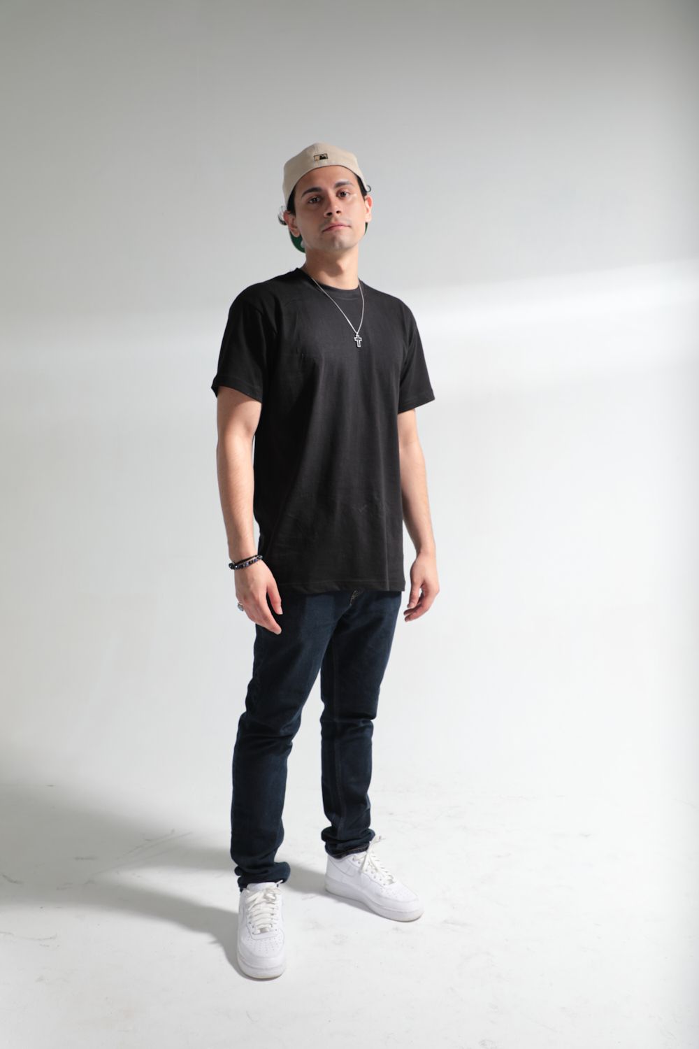 Casual street style outfit with black t-shirt, jeans and white sneakers against plain backdrop.