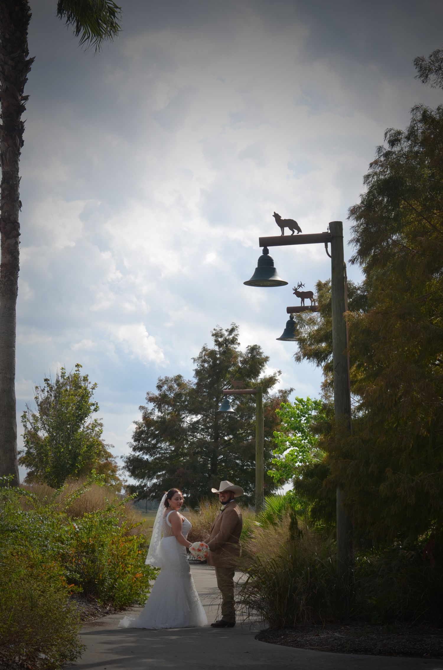 Wedding couple poses under decorative lamp posts with animal silhouettes at sunset.