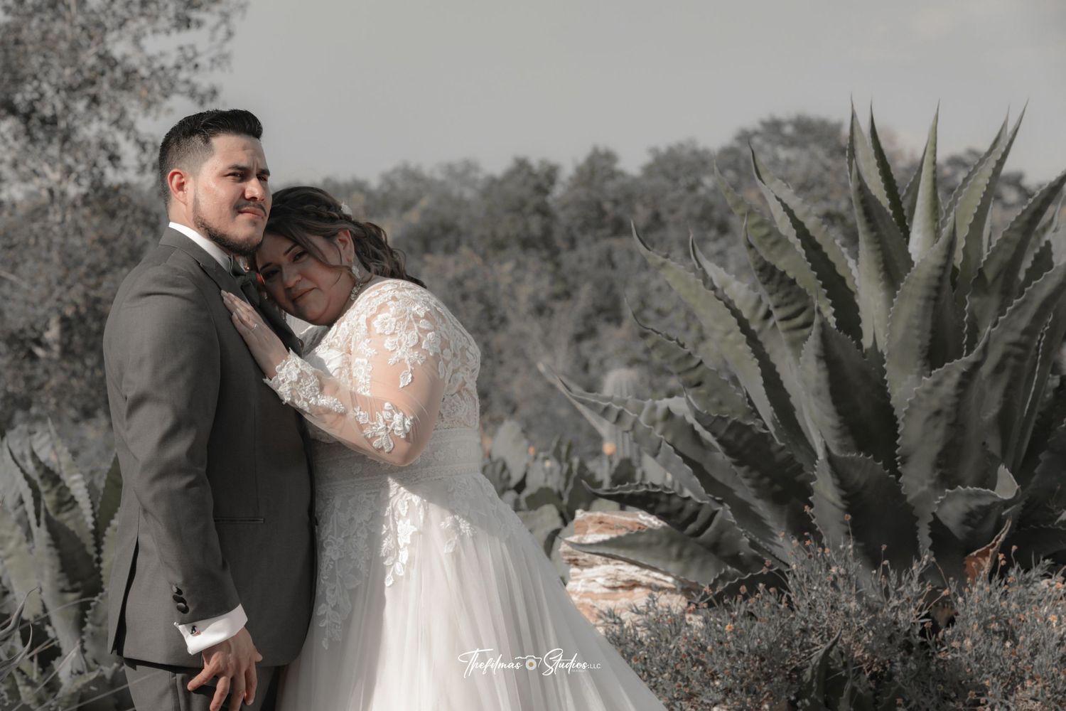 A romantic wedding photo of a couple embracing outdoors with agave plants in the background.