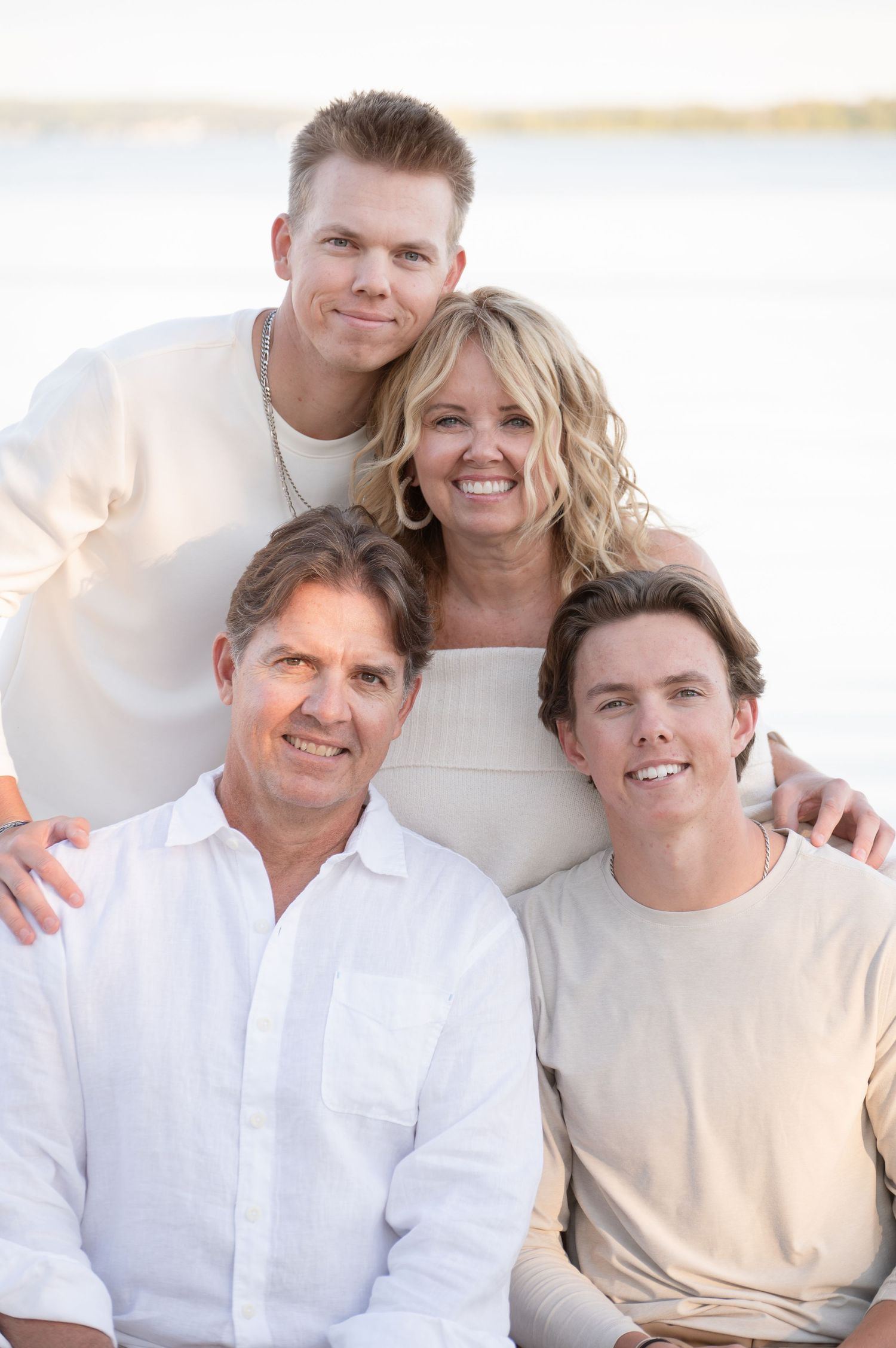 Family dressed in white clothing poses together on bright beach setting.