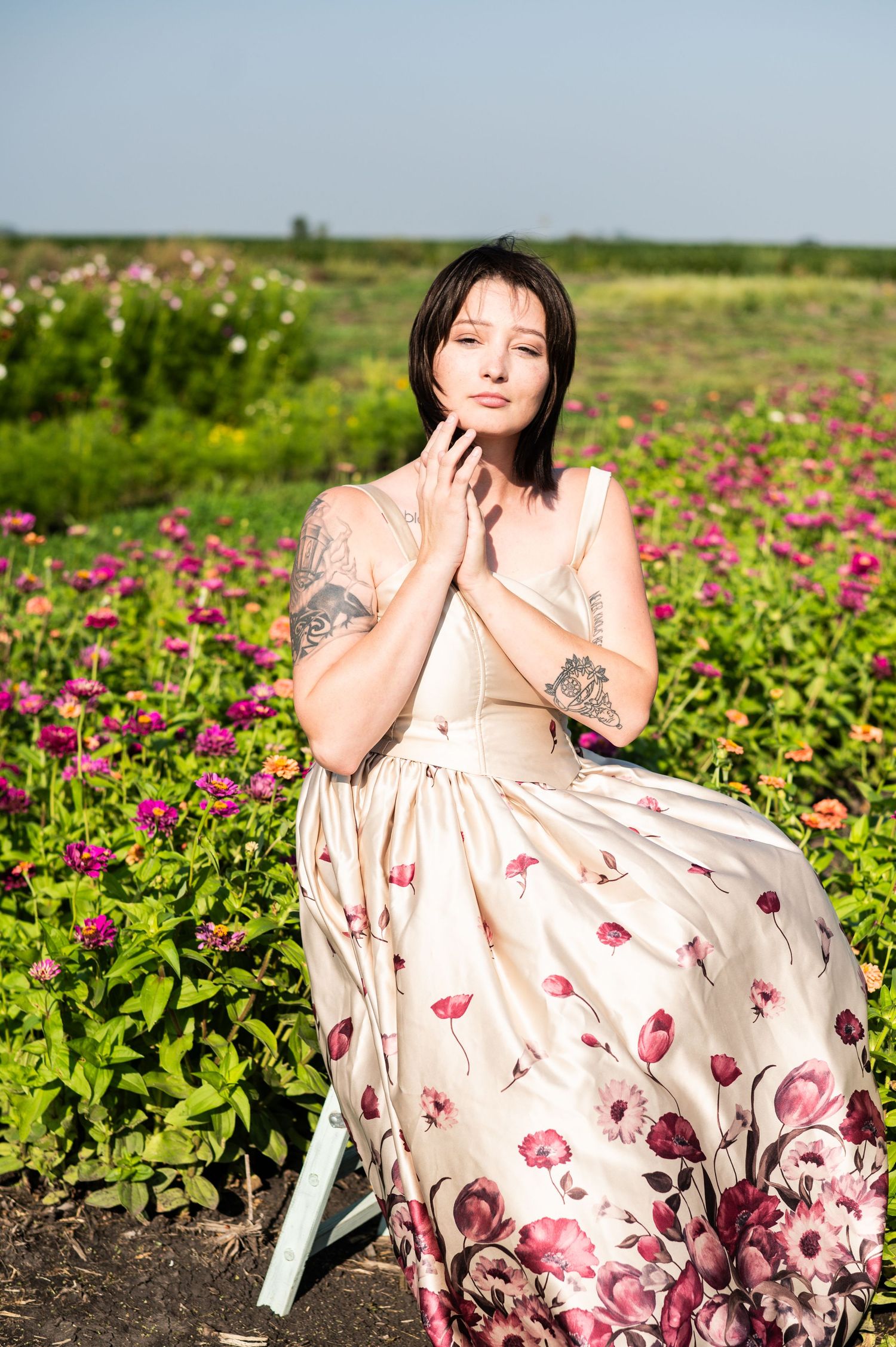 Person in floral dress poses gracefully in field of pink cosmos flowers.