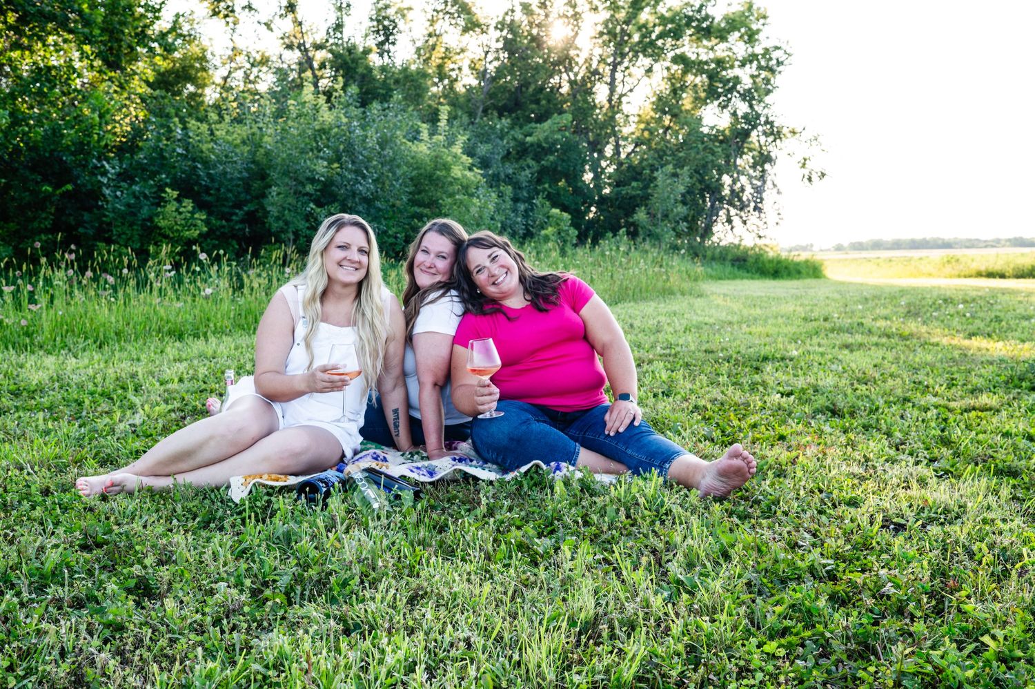 Three friends relax together on a grassy field during golden hour.