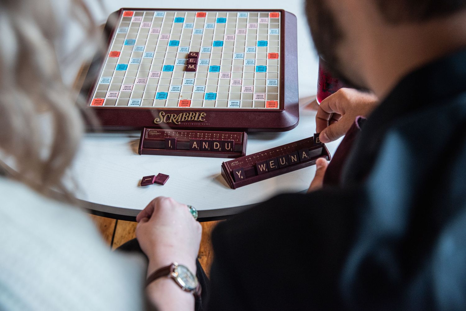 Close-up view of players enjoying a game of Scrabble with wooden letter tiles on the classic board and rack.