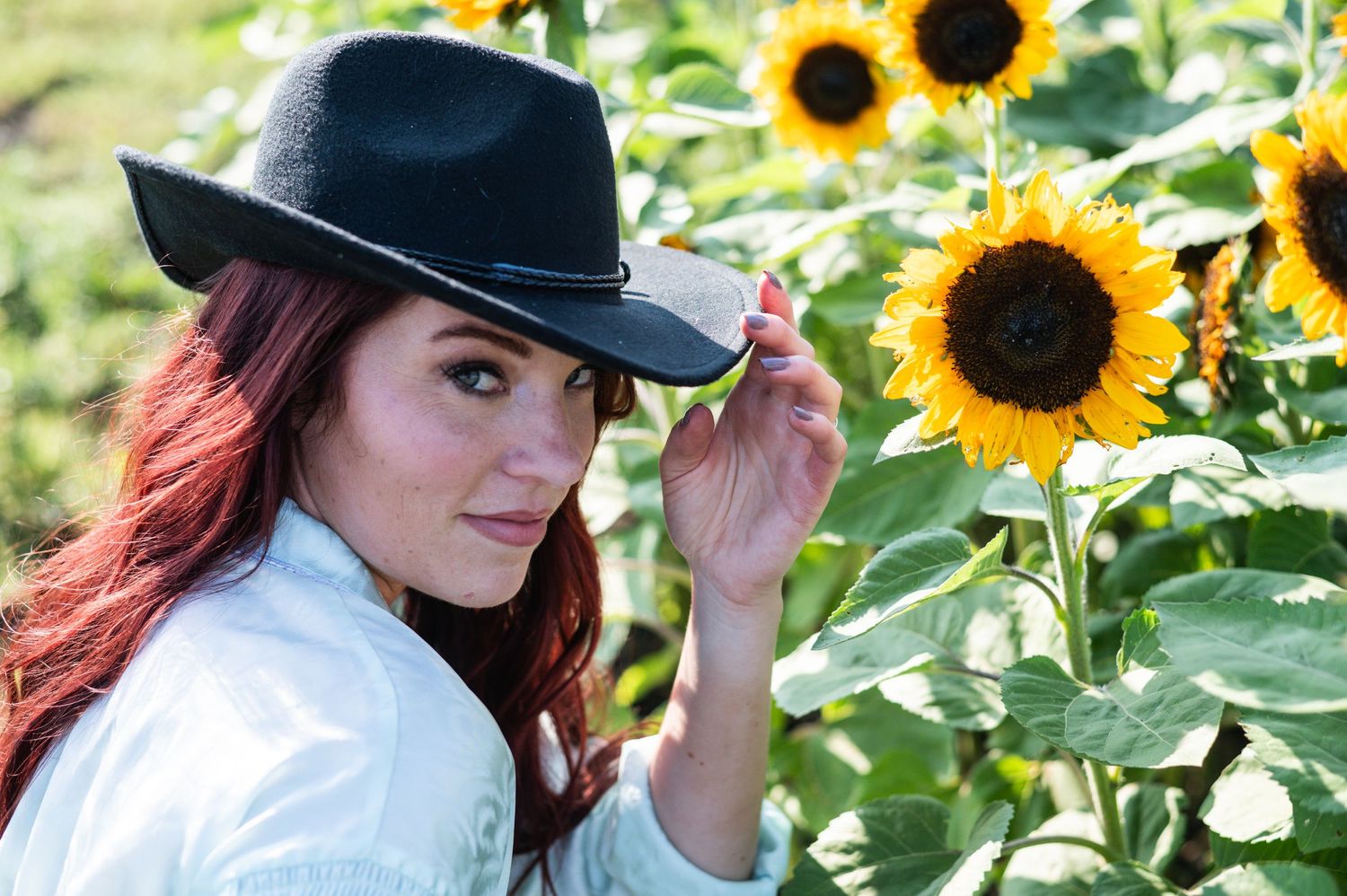 Stylish black hat pose next to bright yellow sunflowers in natural light.
