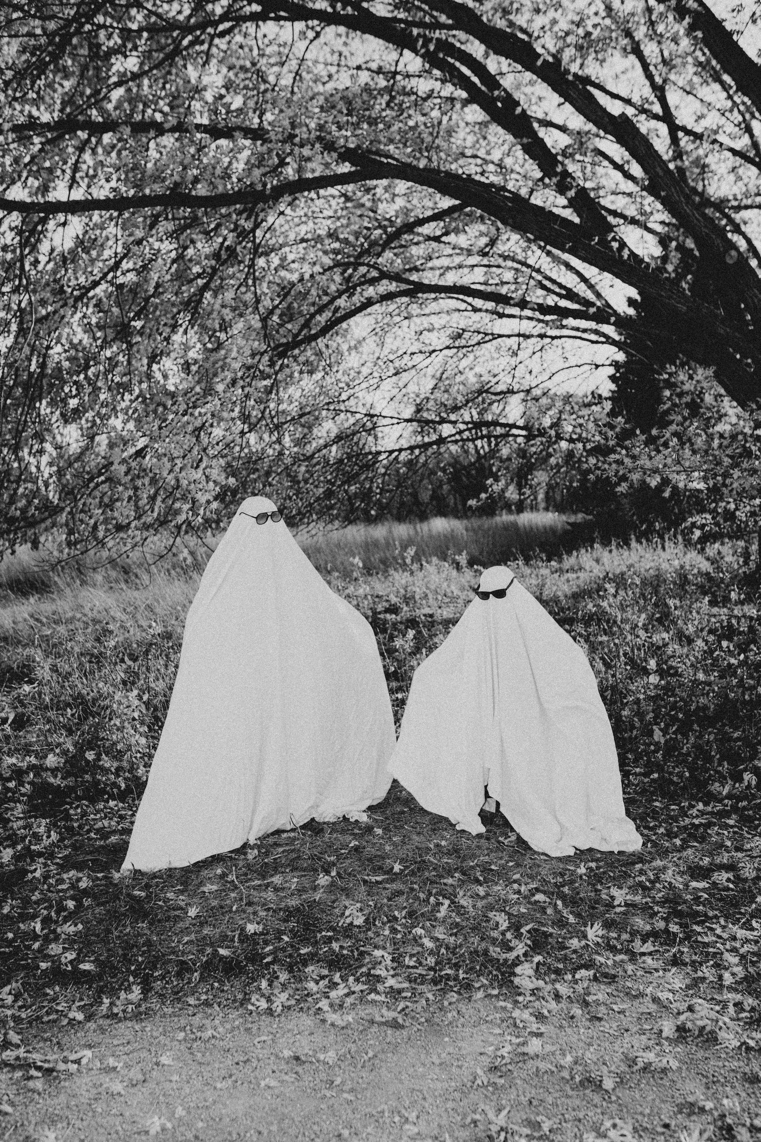 Black and white artistic composition of ghostly figures under tree branches.
