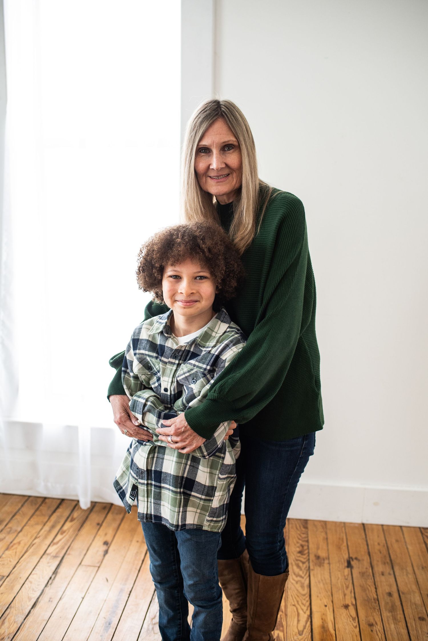 Grandparent and child embracing in a bright room with wooden floors.