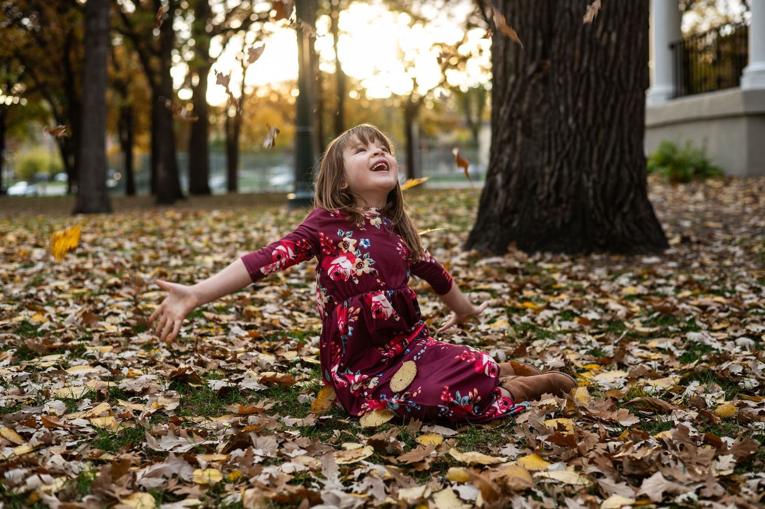 Person lying in fallen autumn leaves enjoying a playful moment outdoors.