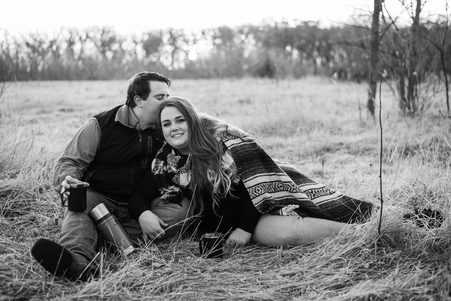 Black and white portrait of a couple relaxing in a rustic field setting.
