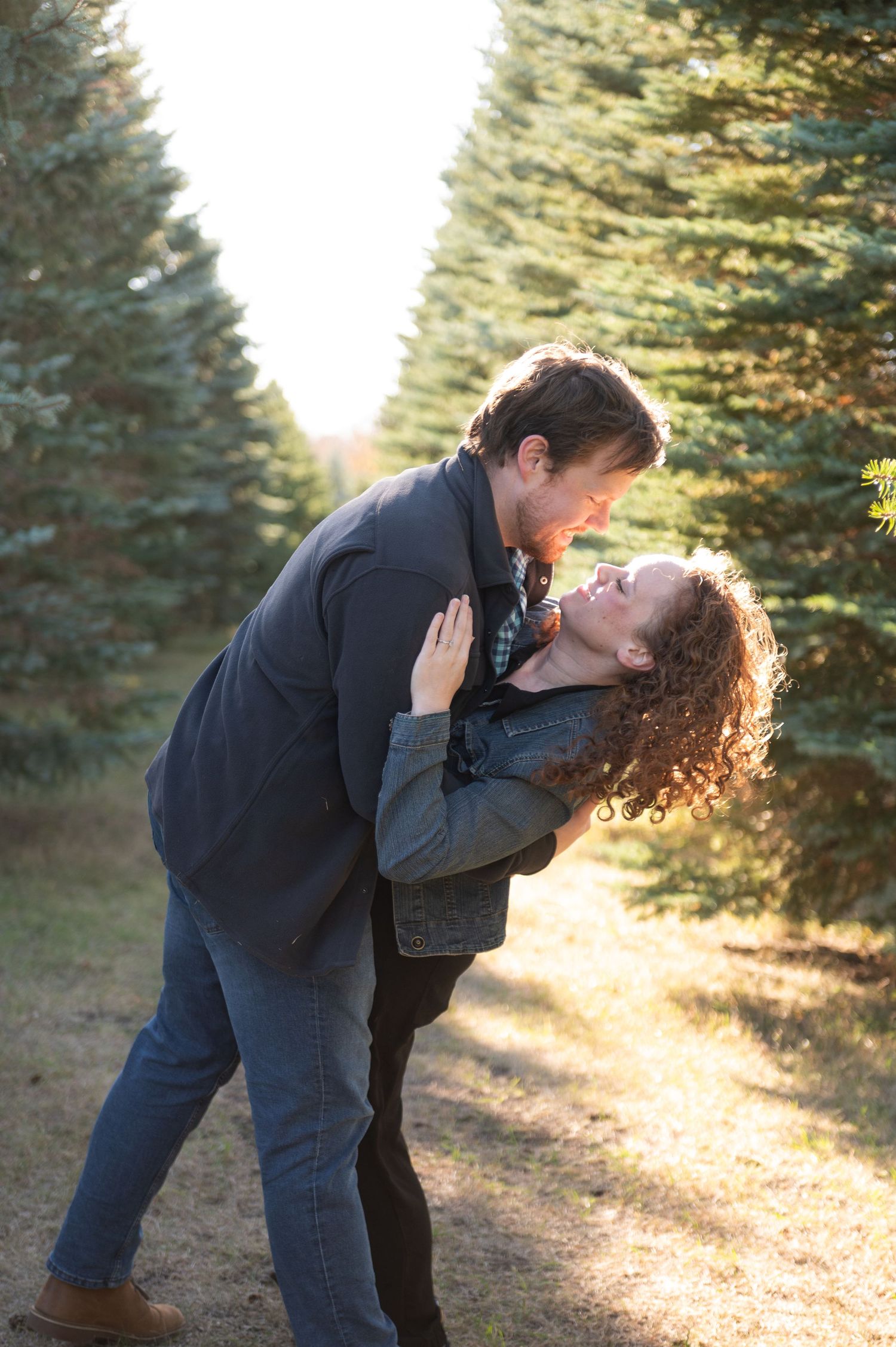 Romantic couple shares a passionate kiss along a sunlit evergreen forest path.