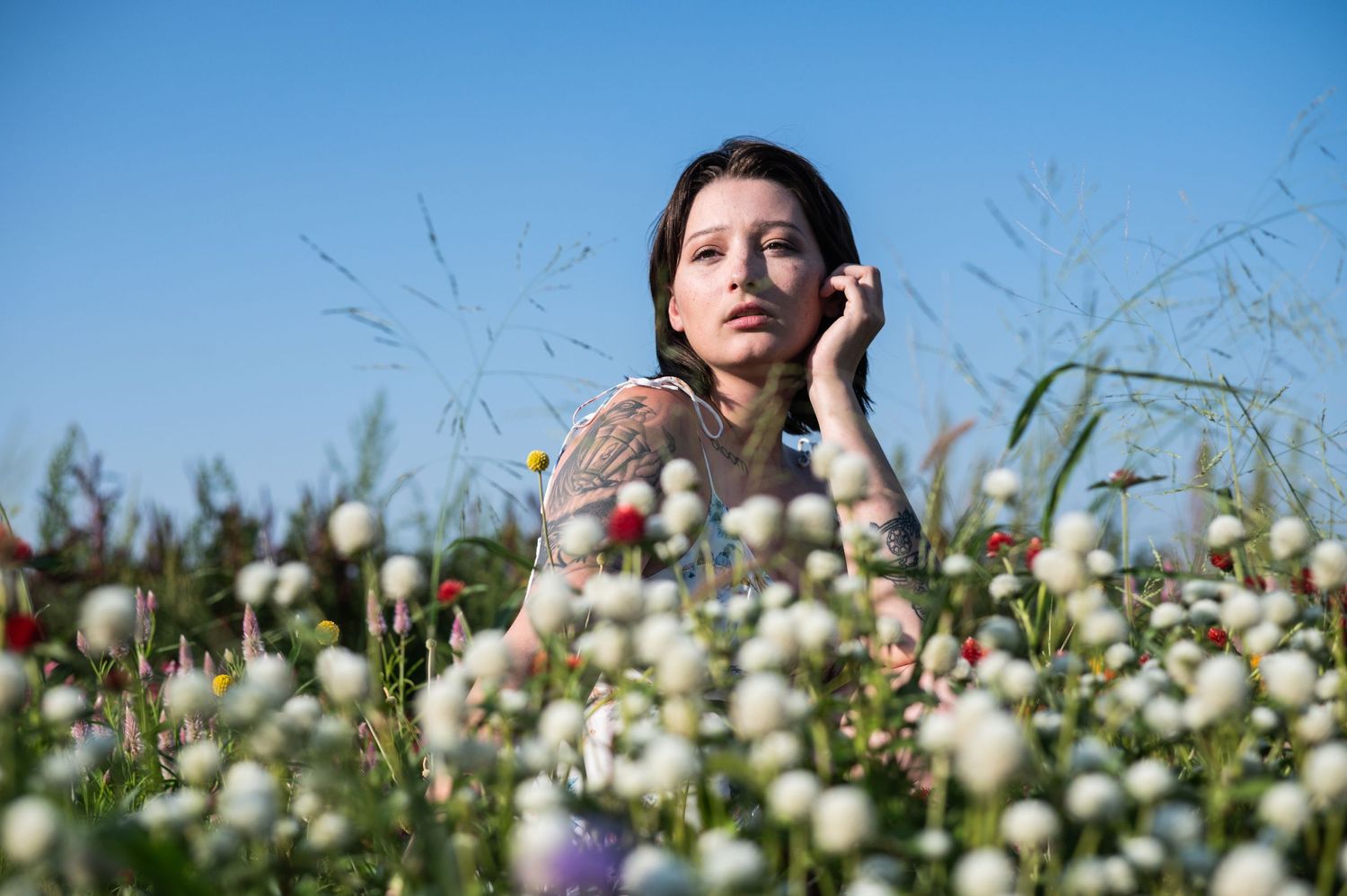 Artistic portrait surrounded by delicate white wildflowers against a blue sky.