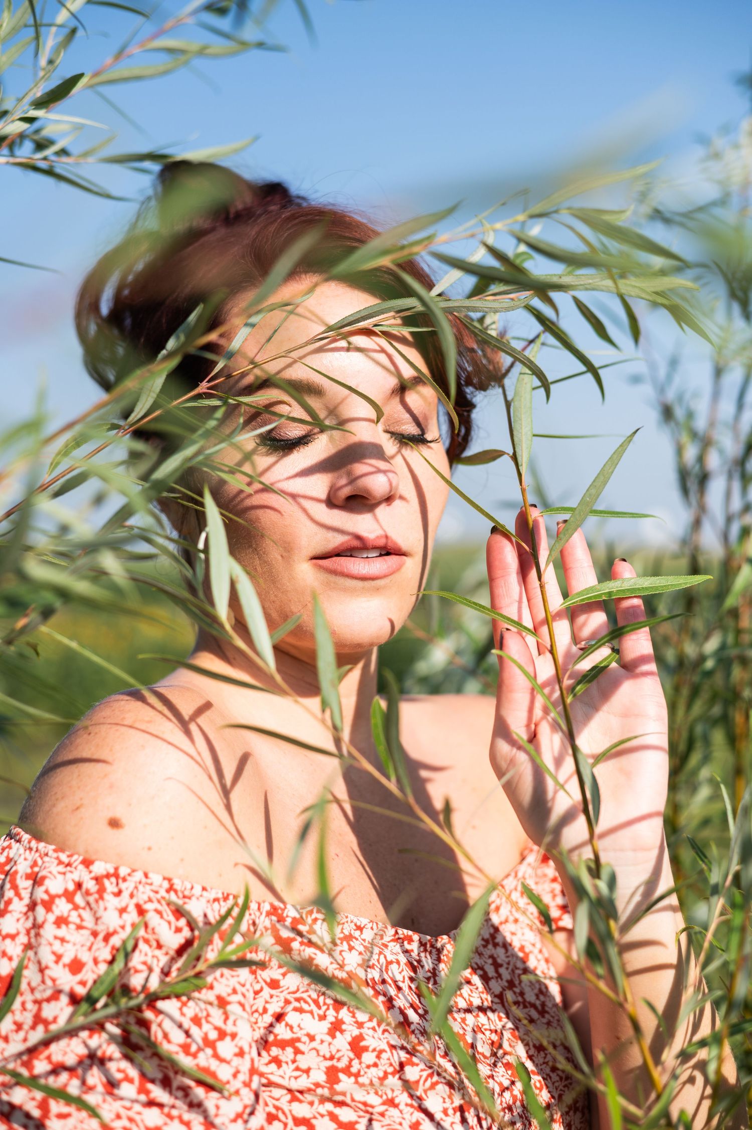 Artistic portrait through bamboo leaves in a floral dress on a sunny day.