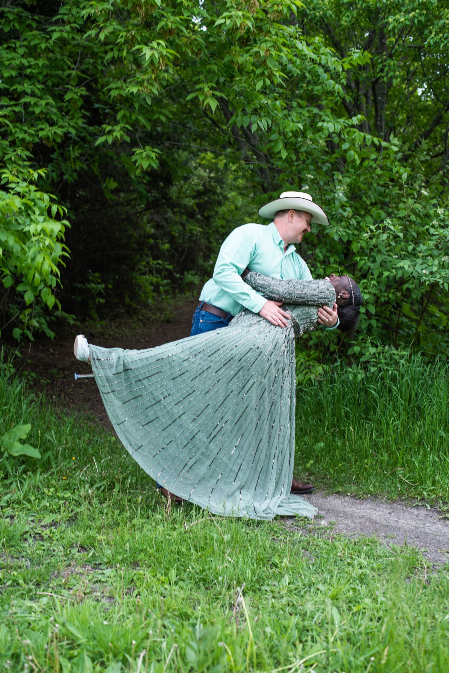 Person in a flowing gray dress and hat twirling gracefully in a garden setting.