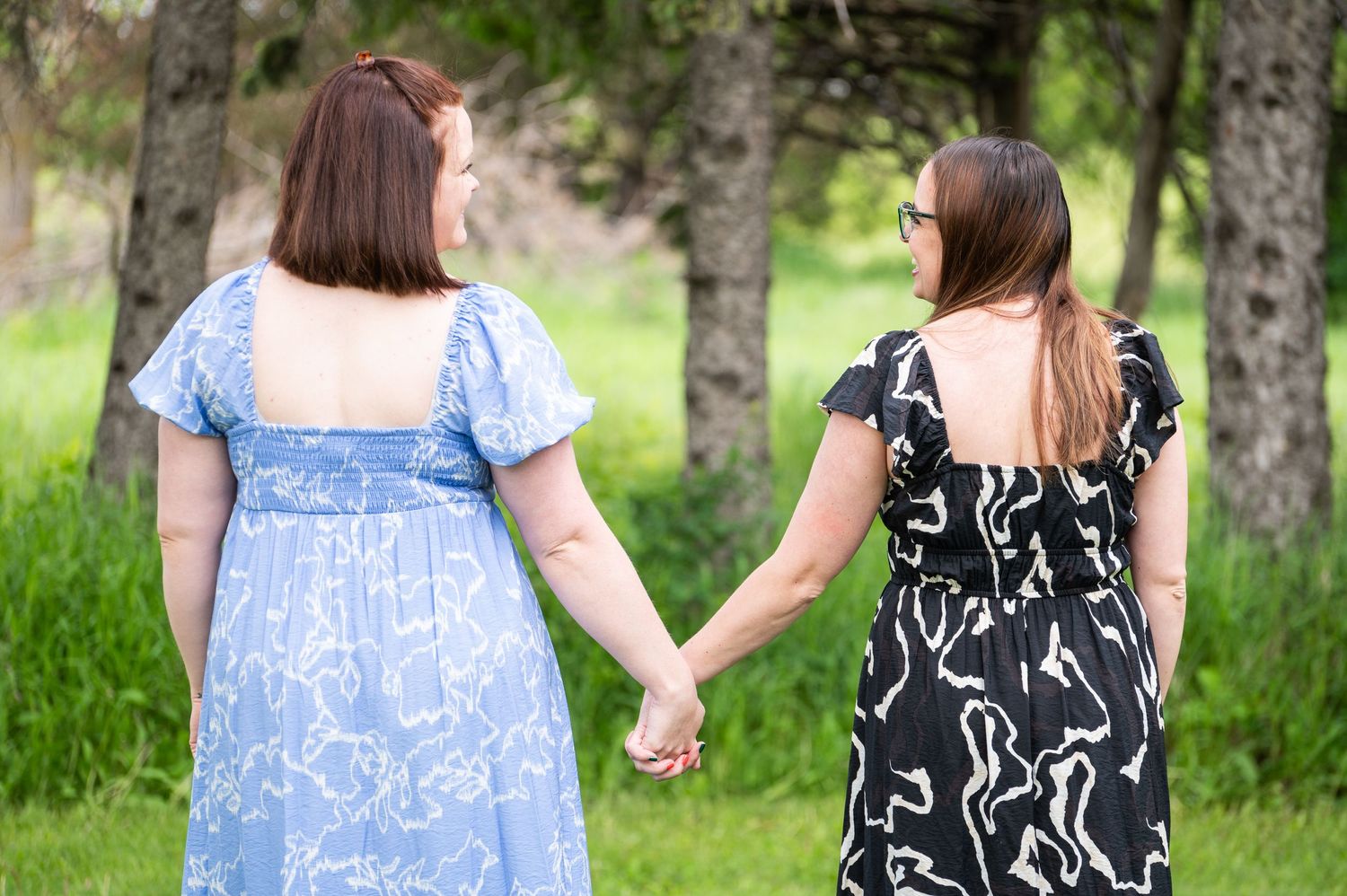 Two people hold hands while walking through a lush green garden.