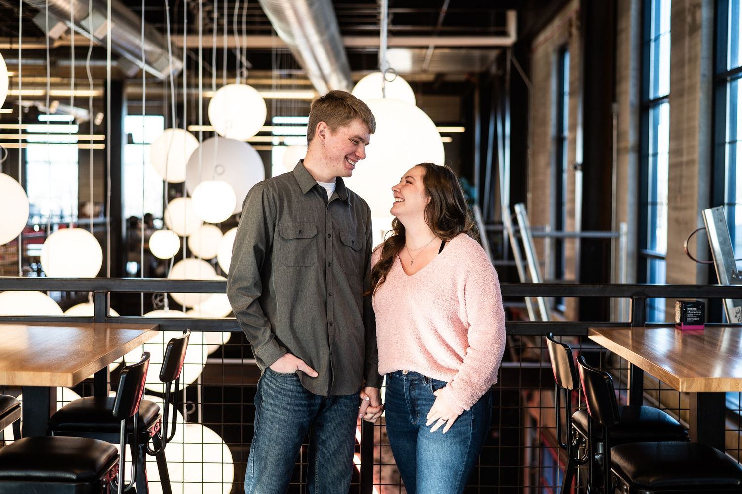 Casual couple standing close together in a modern restaurant with pendant lighting.