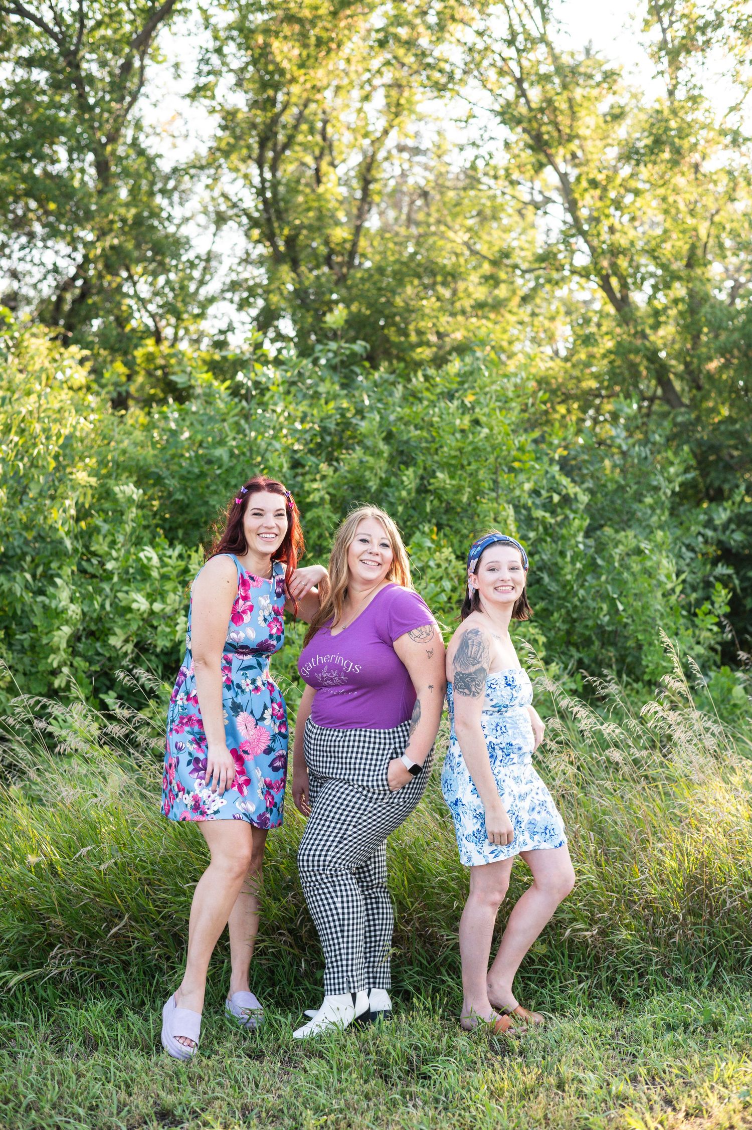 Three friends in summer dresses pose together in a sunlit garden setting.