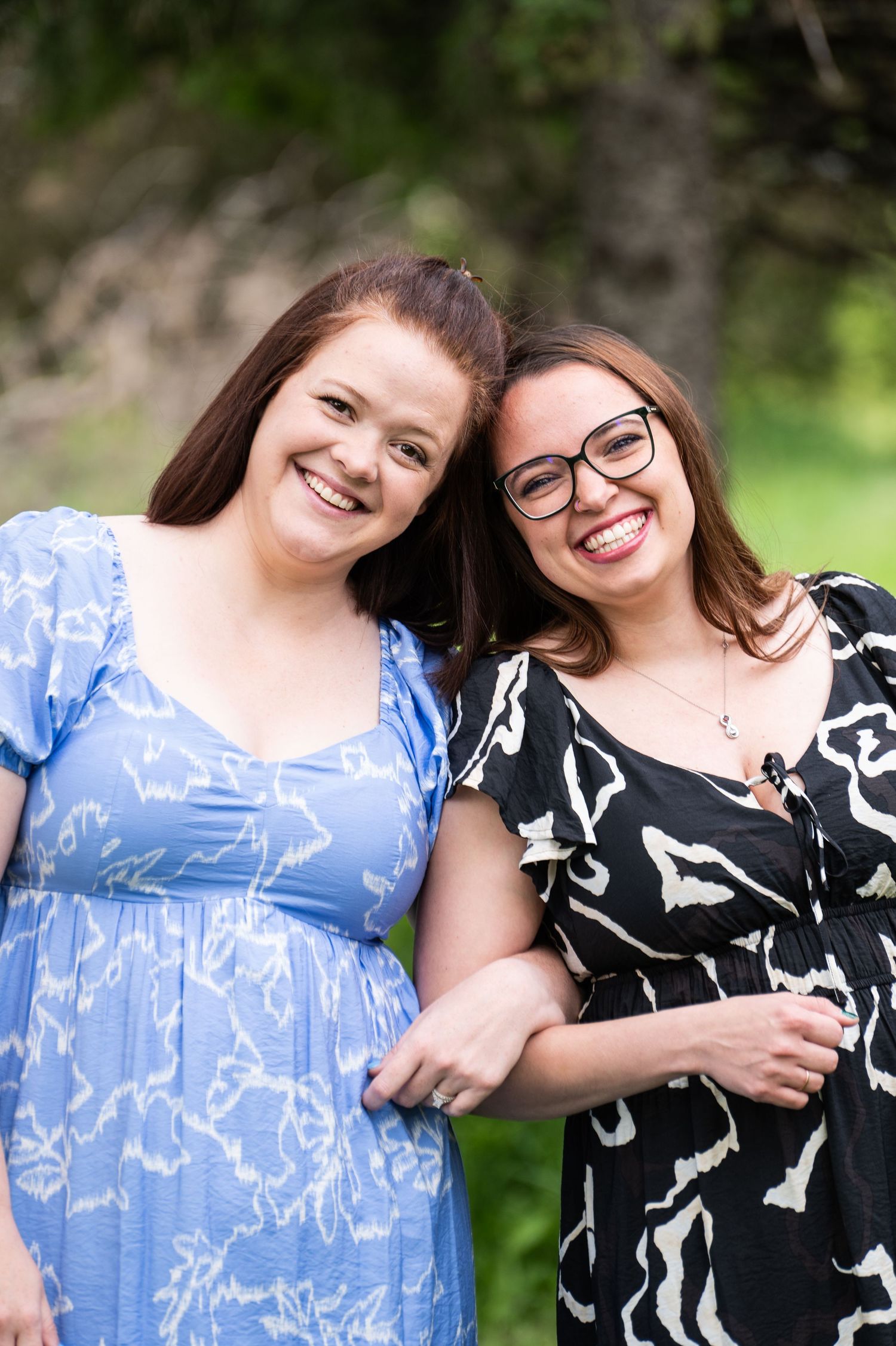 Two friends in summer dresses smile together in a garden setting.