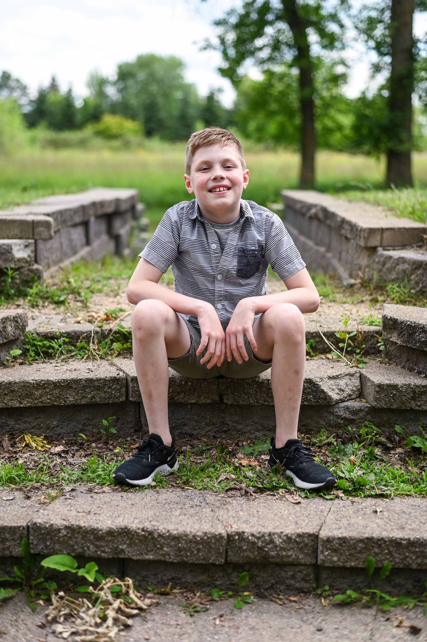 Boy sitting on rustic stone steps outdoors on a sunny summer day.