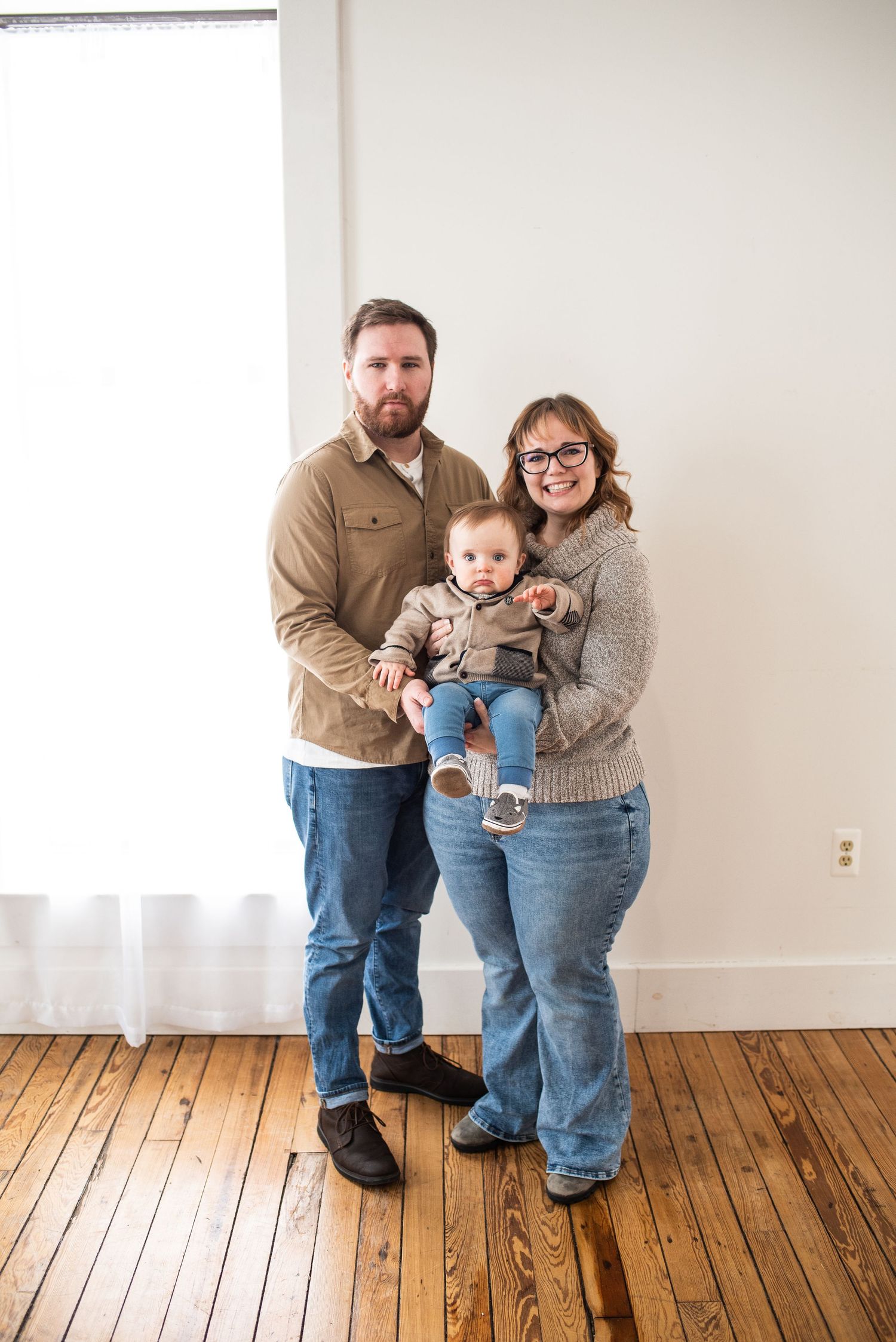 Family members share tender moments on hardwood floors in casual clothing.