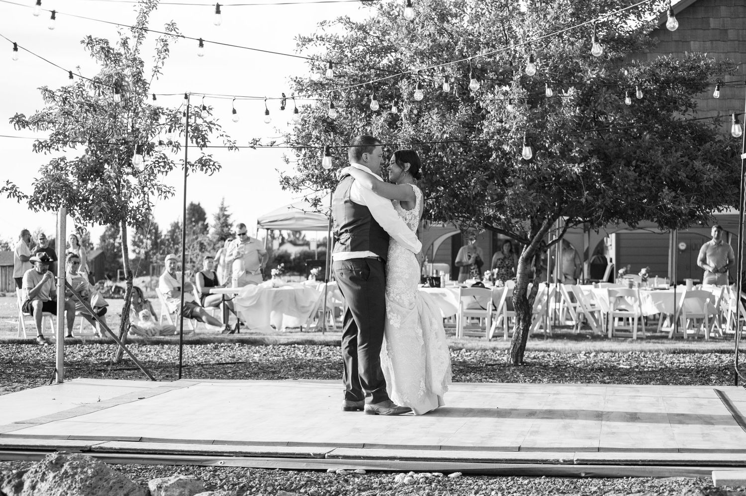 A couple dancing outdoors under string lights in a garden setting.