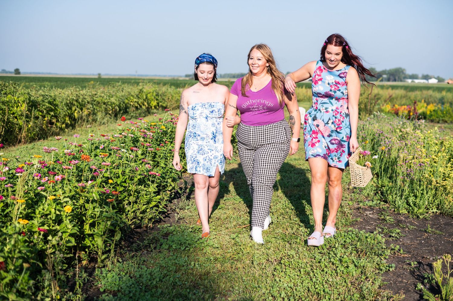Friends walking together through a sunny flower field in colorful summer dresses.