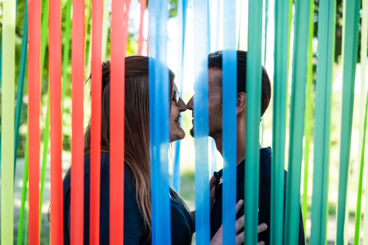 Silhouettes share a kiss behind colorful vertical streamers creating a rainbow effect.