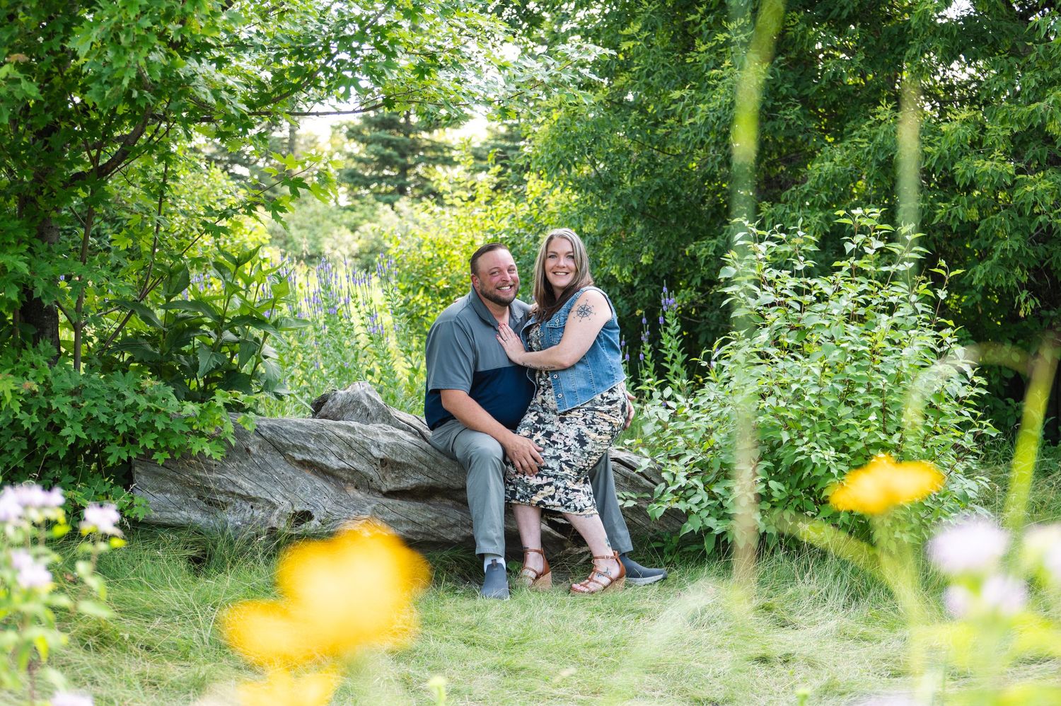 Couple sitting together on rocks in a lush garden setting with yellow wildflowers.