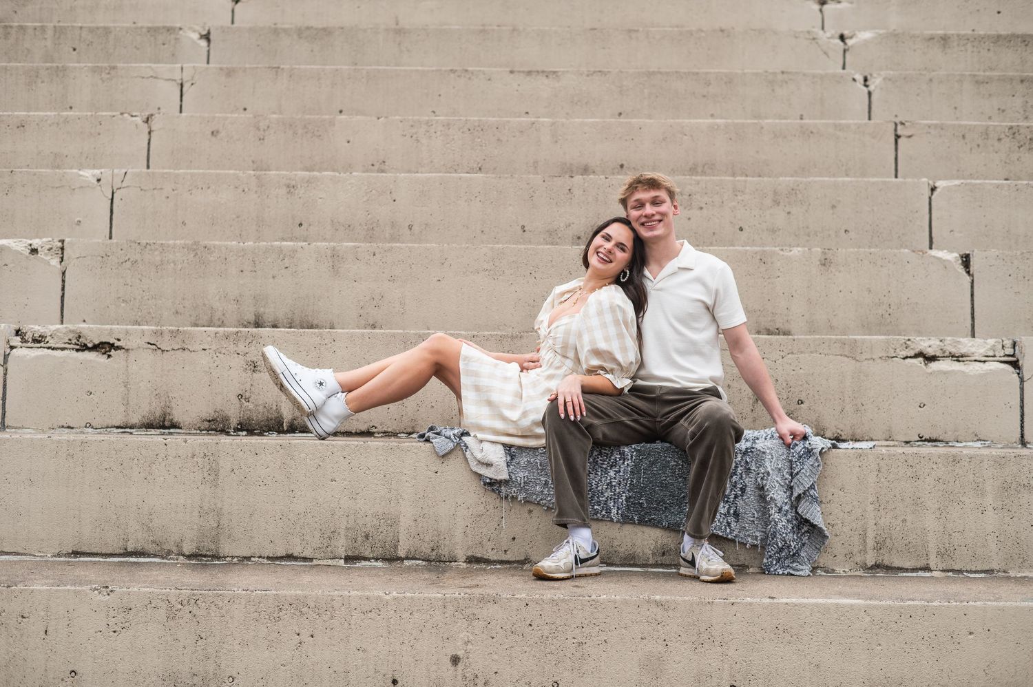A couple poses playfully while laying on concrete steps in a romantic photoshoot.