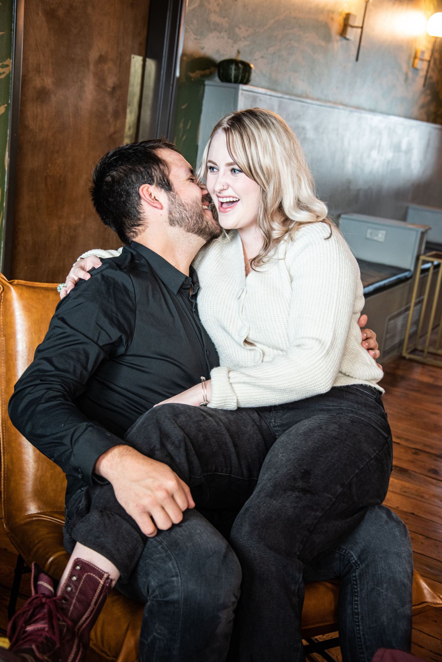 A romantic moment shared between a couple on a leather couch in a dimly lit room.